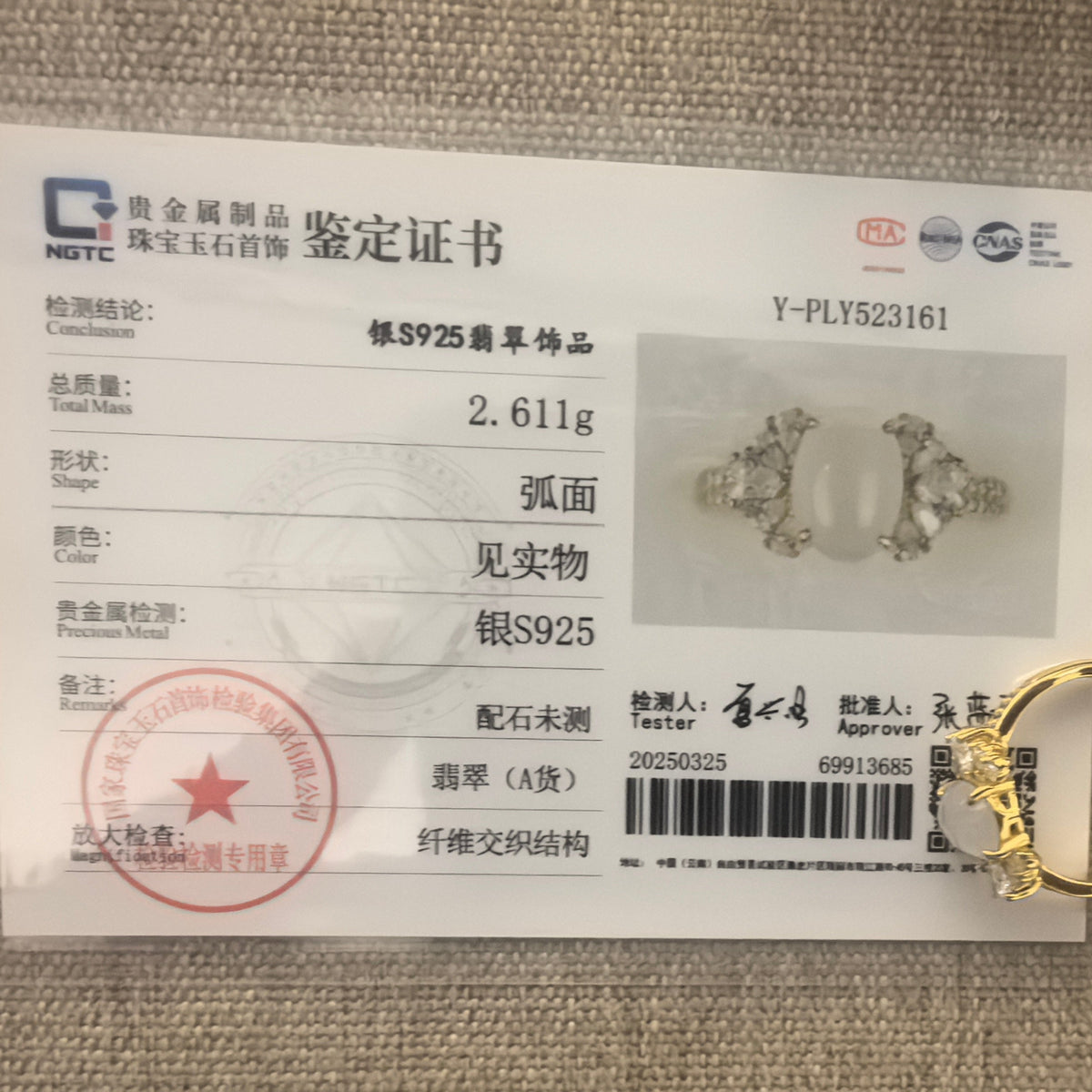 White jadeite ring beside its matching NGTC certificate on a woven background.
