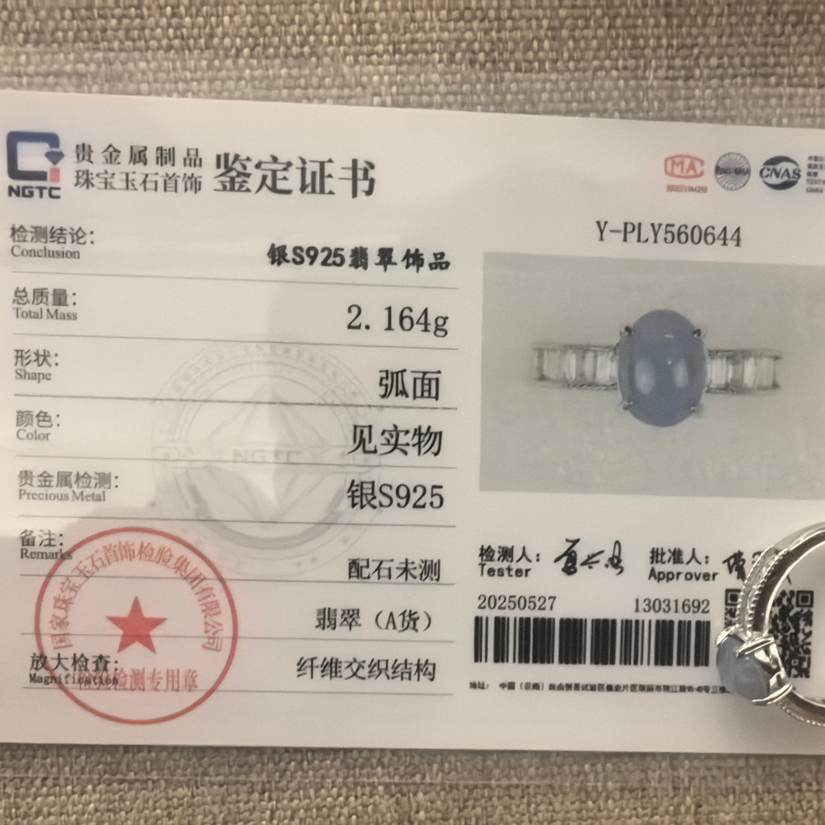 Purple oval jadeite ring in S925 sterling silver beside its matching NGTC certificate on a woven background.