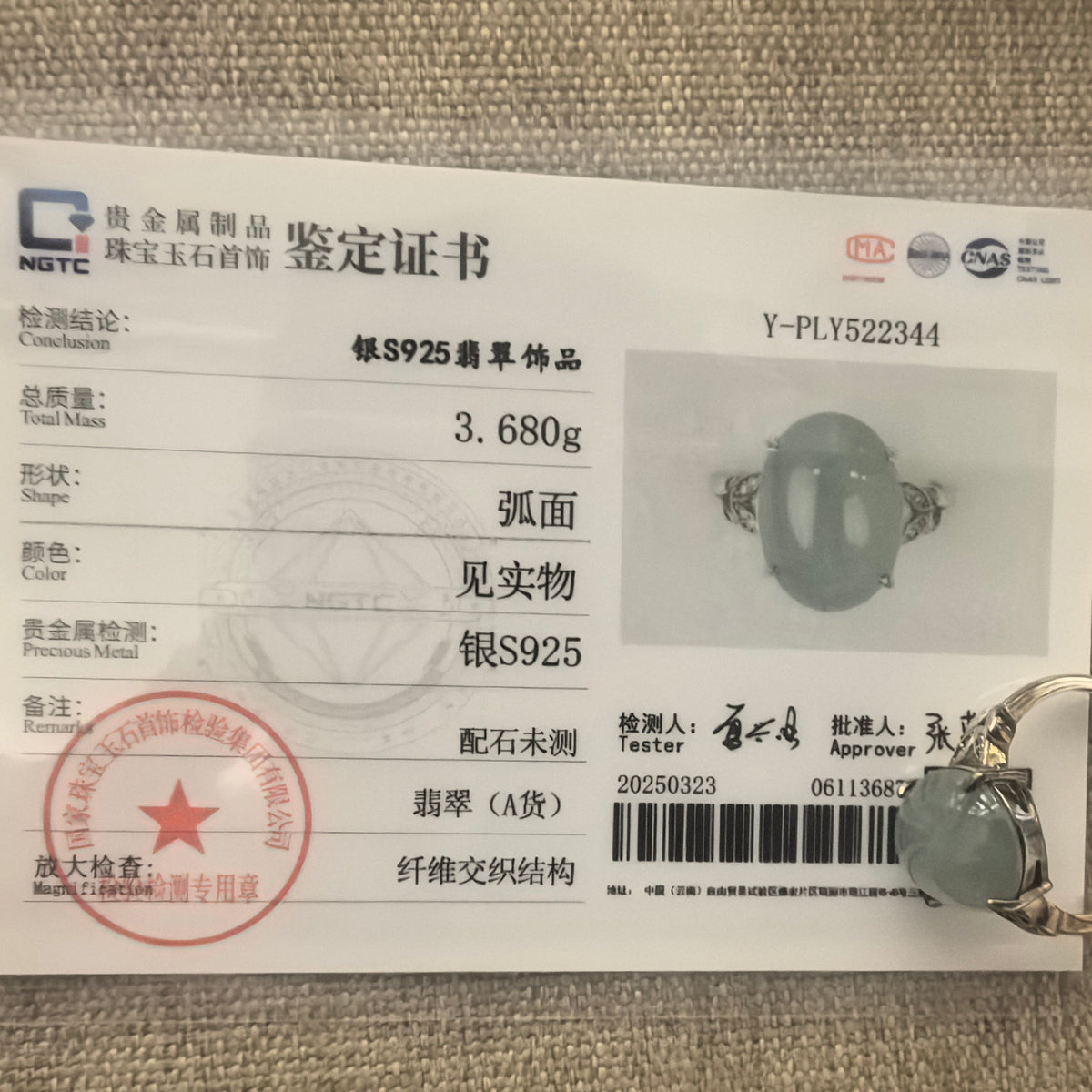 S925 sterling silver lake green jadeite ring beside its matching NGTC certificate on a woven background.