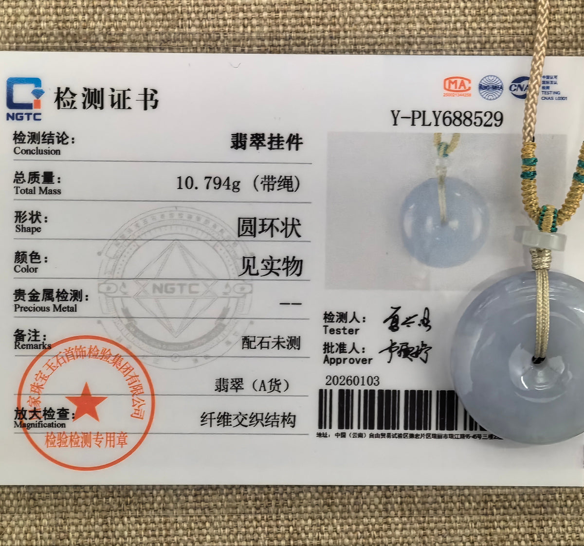Blue-lavender jadeite Peace Pendant beside its matching NGTC certificate numbered Y-PLY688529, with the braided cord and pale spacer bead visible.