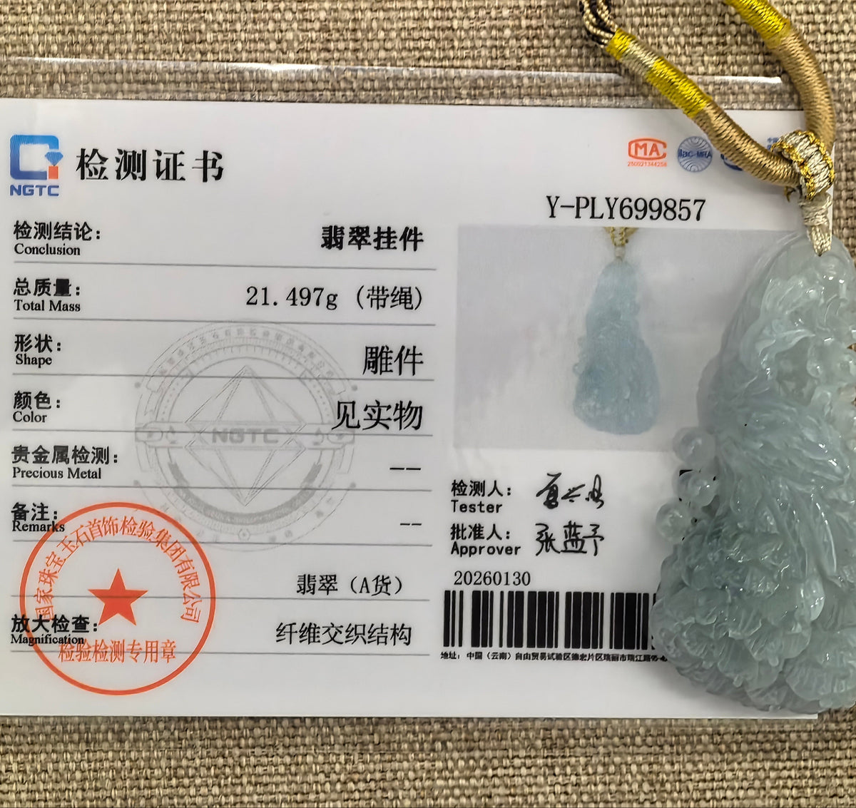 Blue jadeite Phoenix Pendant with a decorative cord beside its matching NGTC certificate on a woven background.
