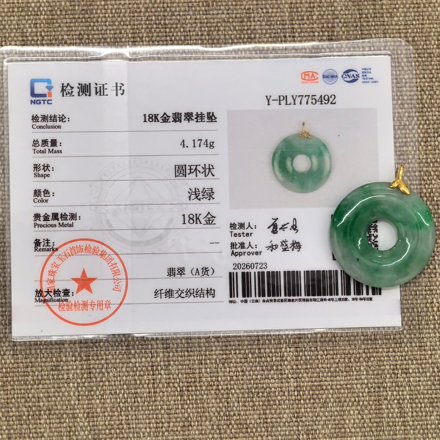 NGTC-certified white-base green jadeite donut pendant displayed with its matching certificate and 18K gold fitting.