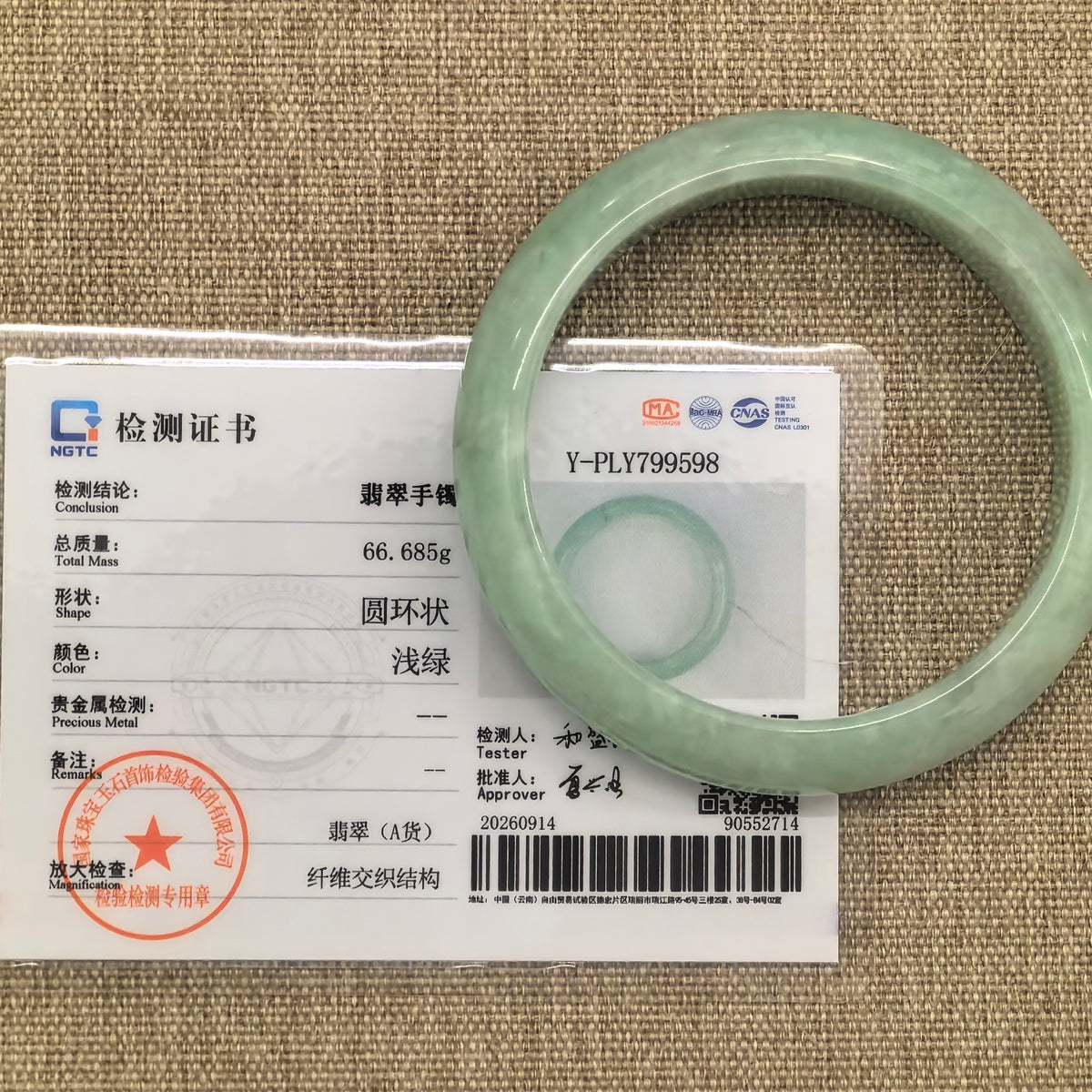 Apple green jadeite bangle displayed with its matching NGTC certificate on a woven background.