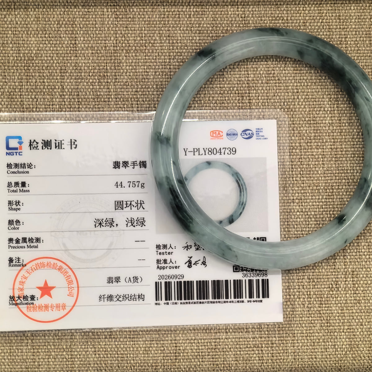 Deep green floating pattern jadeite round-bar bangle displayed over its matching NGTC Grade-A jadeite certificate.