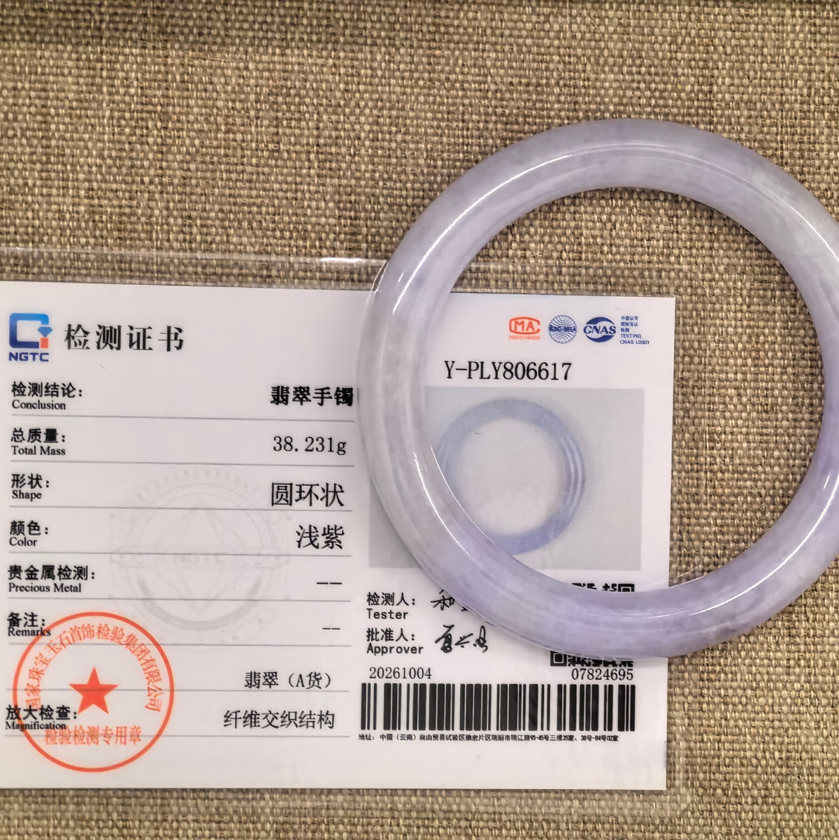 Lavender round-bar jadeite bangle displayed with its matching NGTC certificate on a woven background.