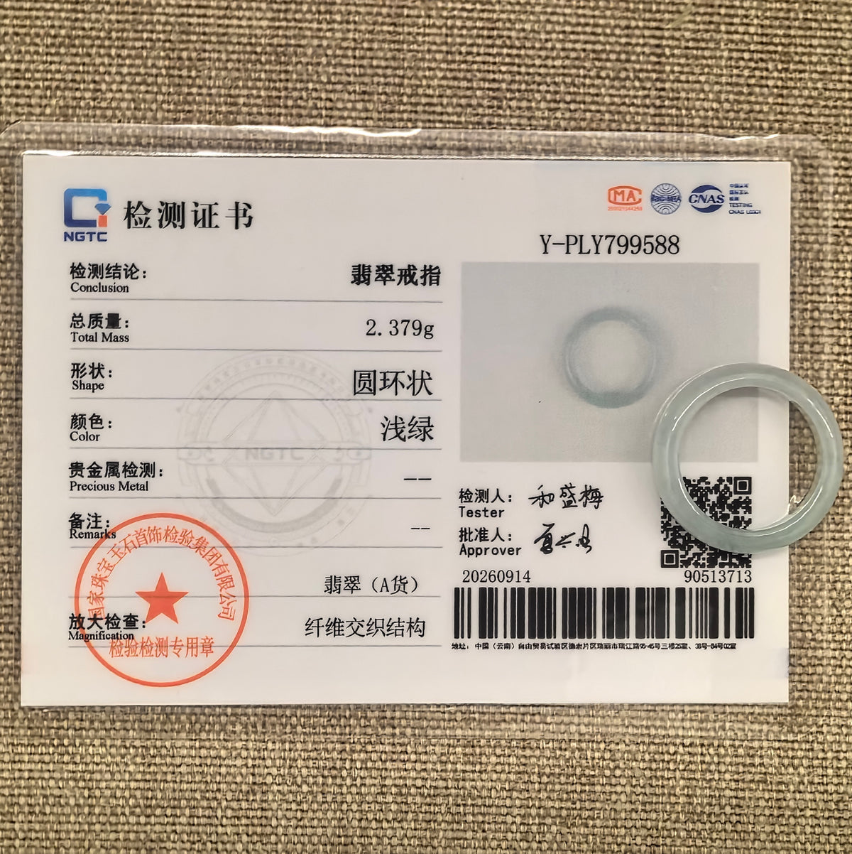 White jadeite ring band displayed with its matching NGTC certificate on woven fabric.