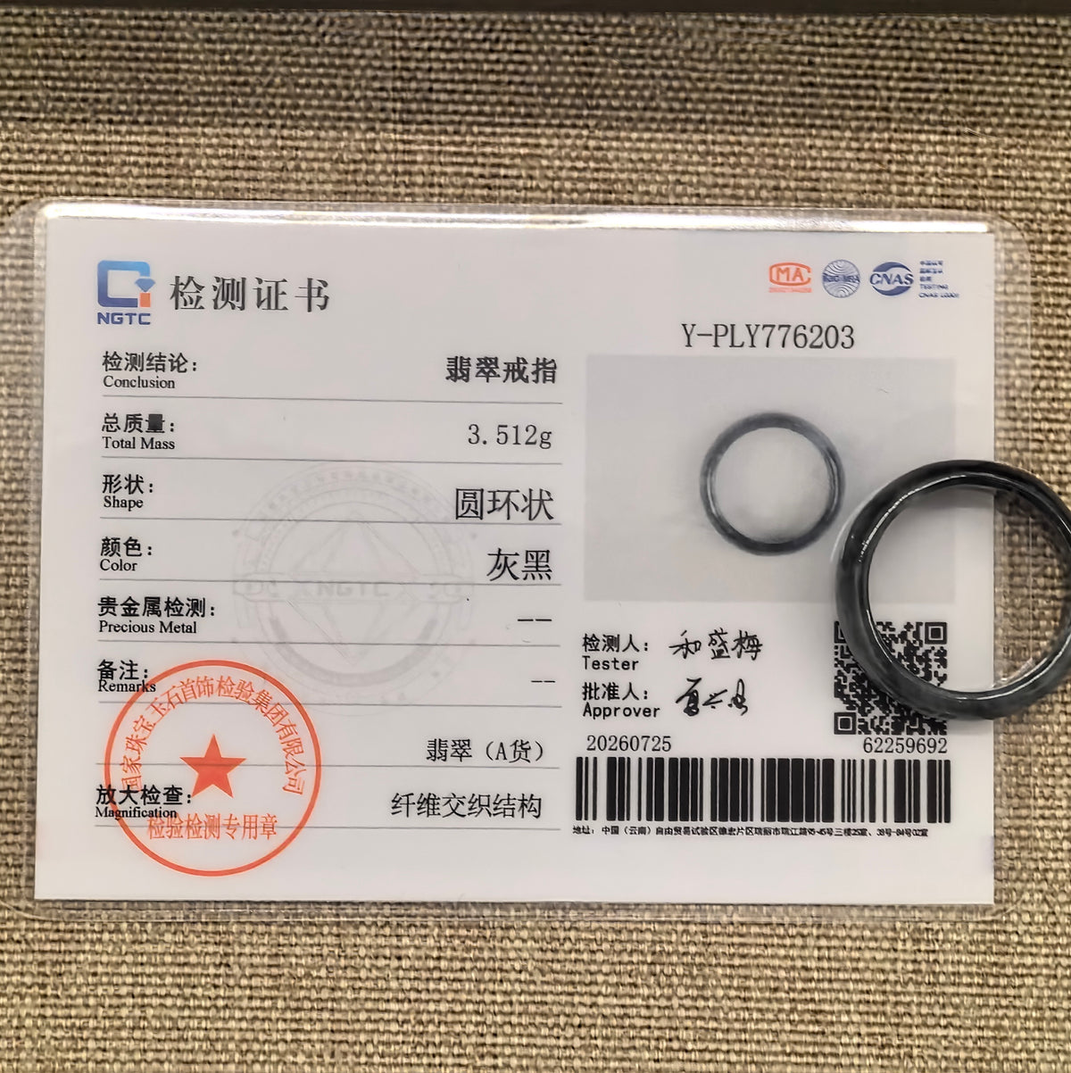 Gray-black jadeite ring band displayed with its matching NGTC certificate on woven fabric.