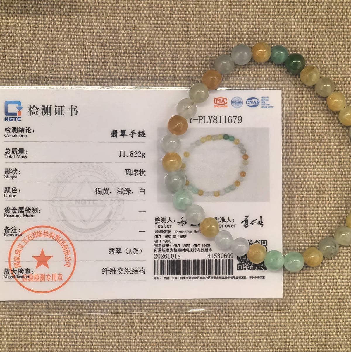 Multicolor jadeite bead bracelet displayed with its matching NGTC certificate on woven fabric.