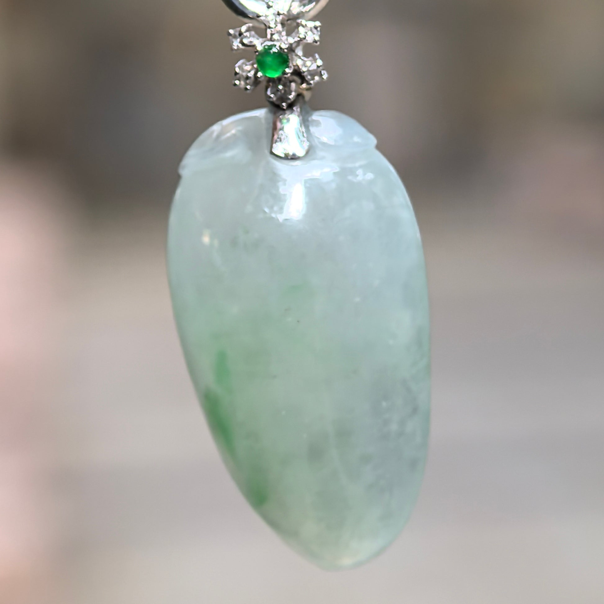 Close-up of light green melon jadeite pendant showing curved carving, soft translucency, and 18K gold setting.