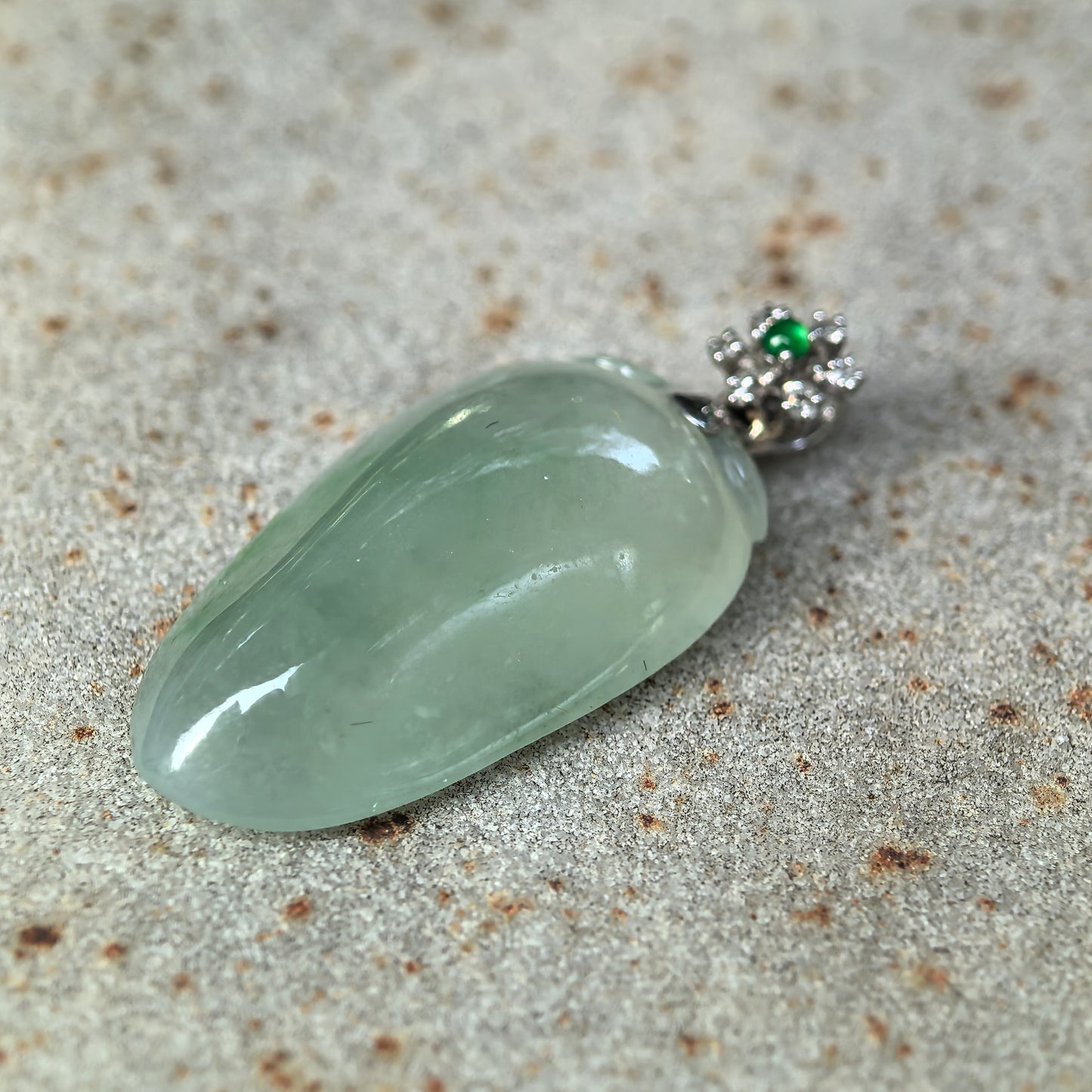 Side view of icy glutinous light green jadeite melon pendant showing thickness and rounded curved surface.
