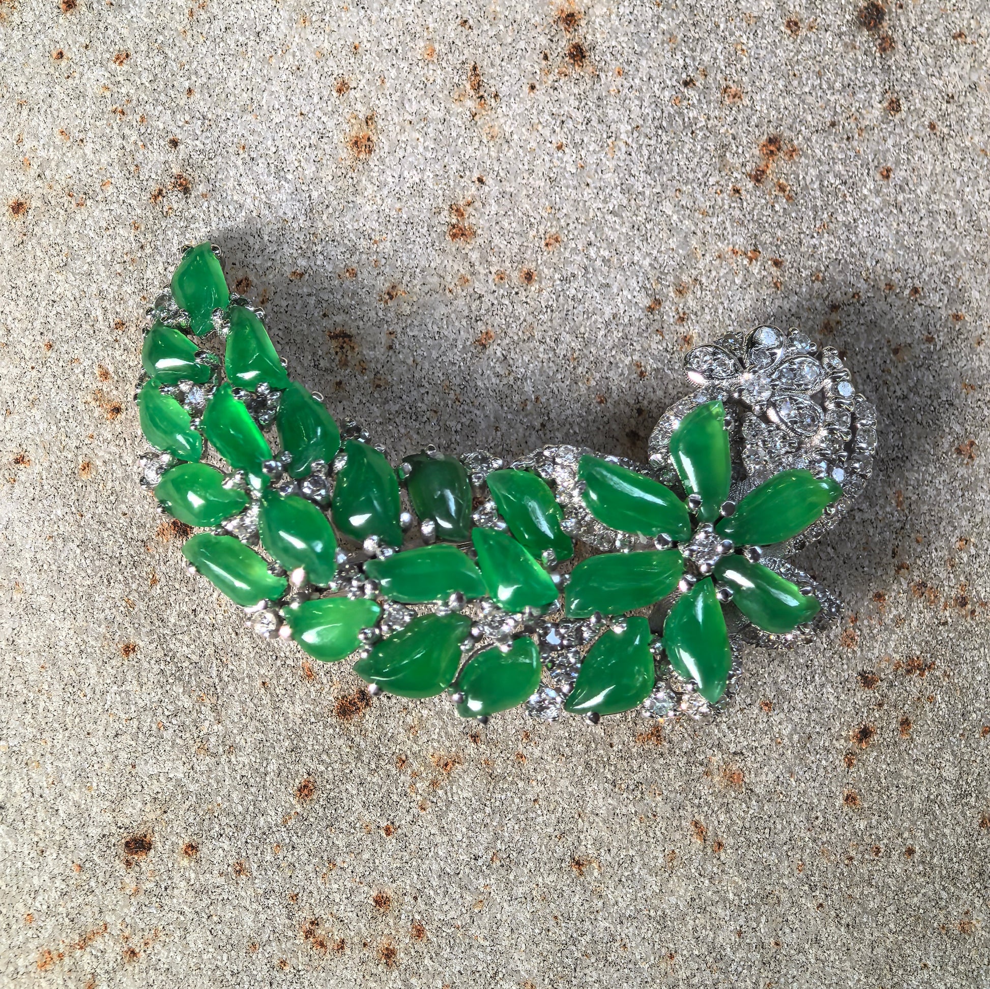 Natural Grade-A icy green 18K gold jadeite brooch with diamond accents displayed on stone background.