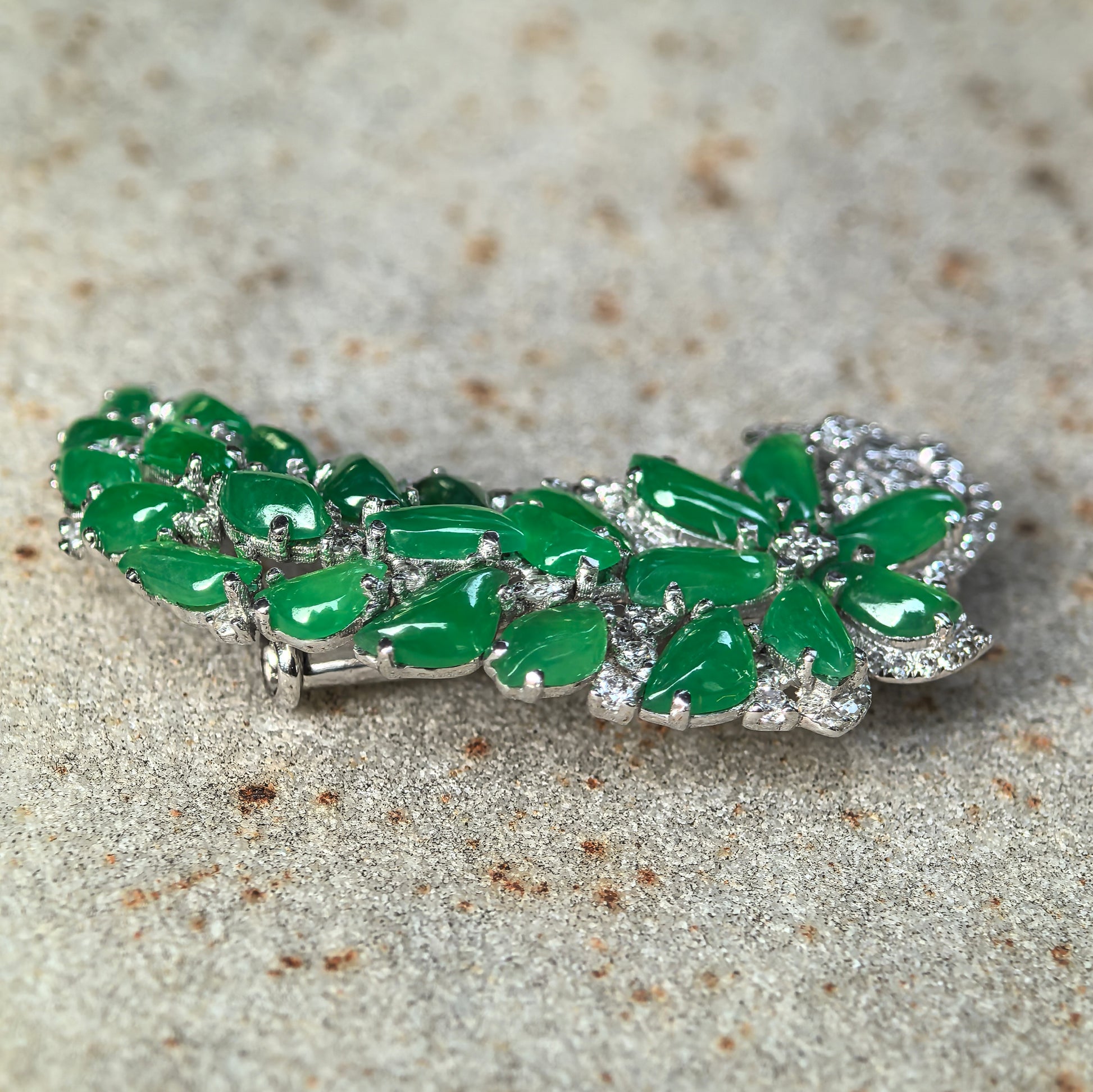 Angled view of vivid green multi-stone jadeite brooch with polished icy texture and 18K gold setting.