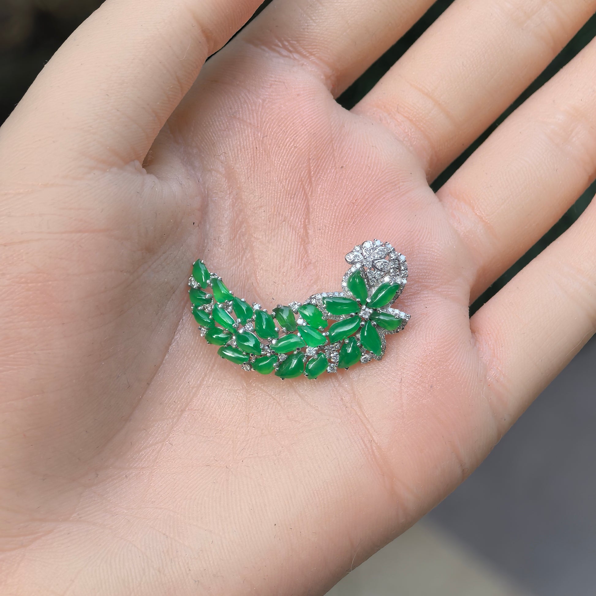Natural Grade-A icy green jadeite brooch shown in hand with curved floral vine design.