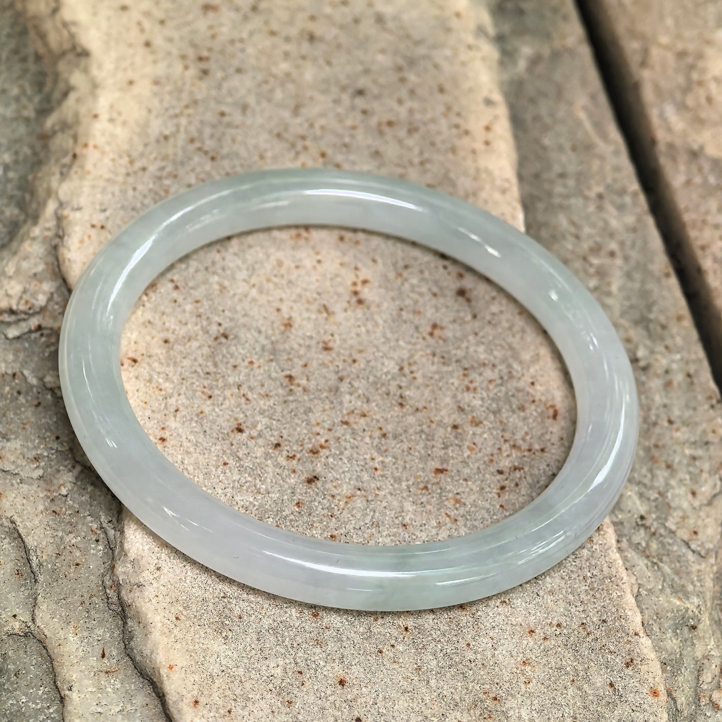 Side view of slim light green jadeite bangle showing polished round profile and good translucency.