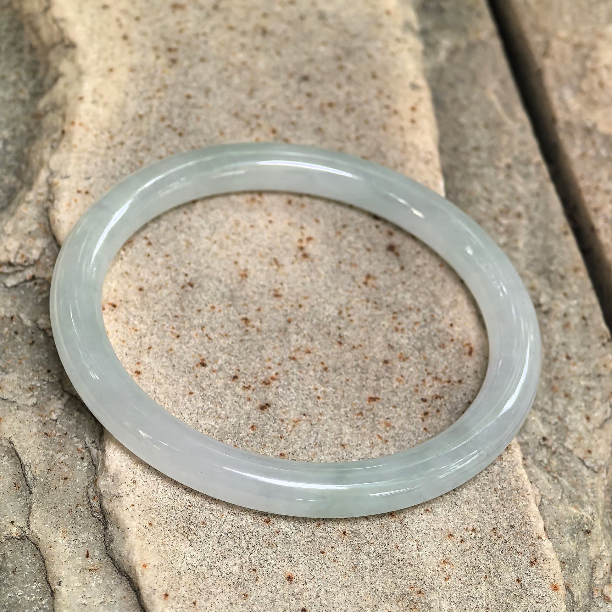 Side view of slim light green jadeite bangle showing polished round profile and good translucency.