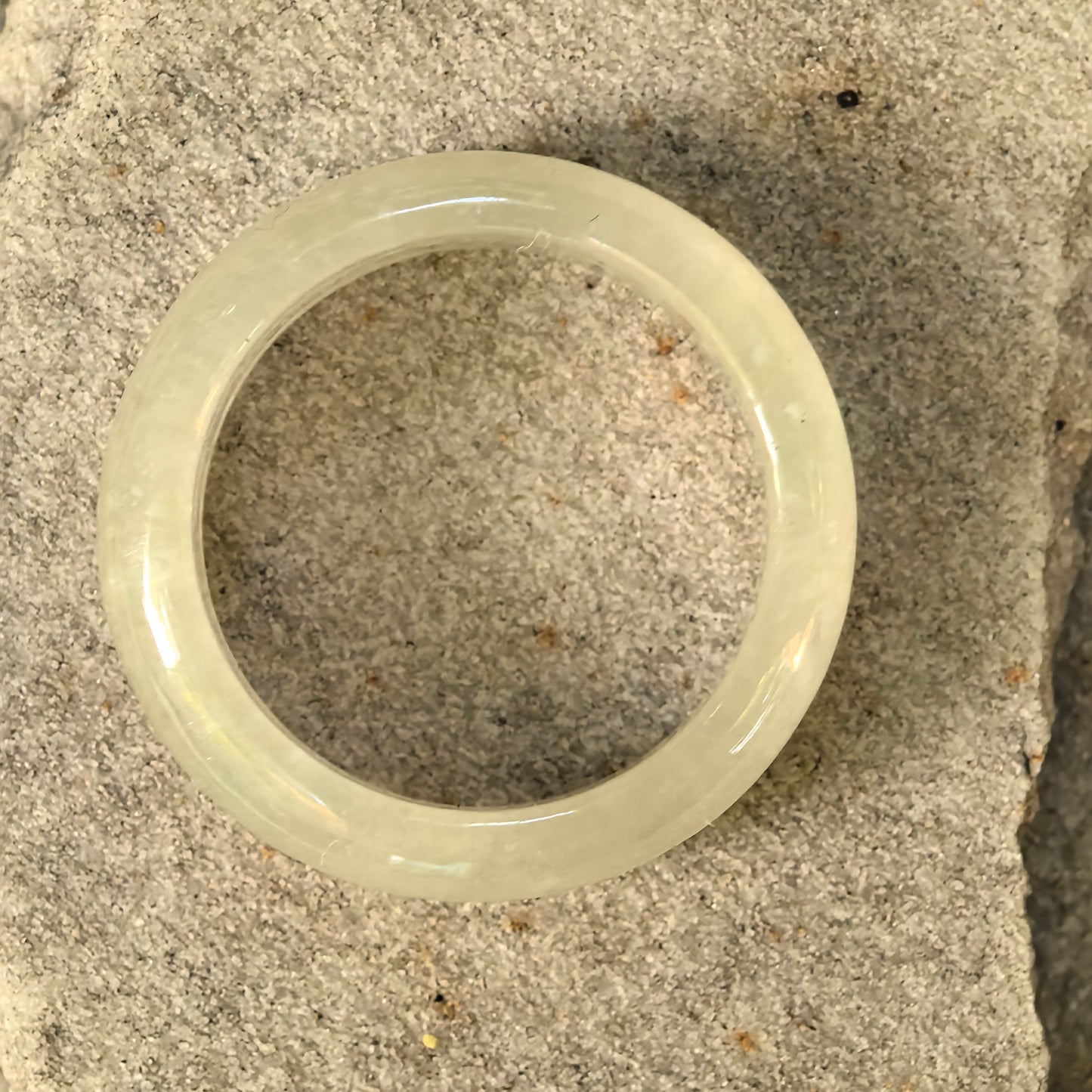 Natural Grade-A yellow jadeite ring band placed on stone surface, showing circular shape and icy glutinous texture.
