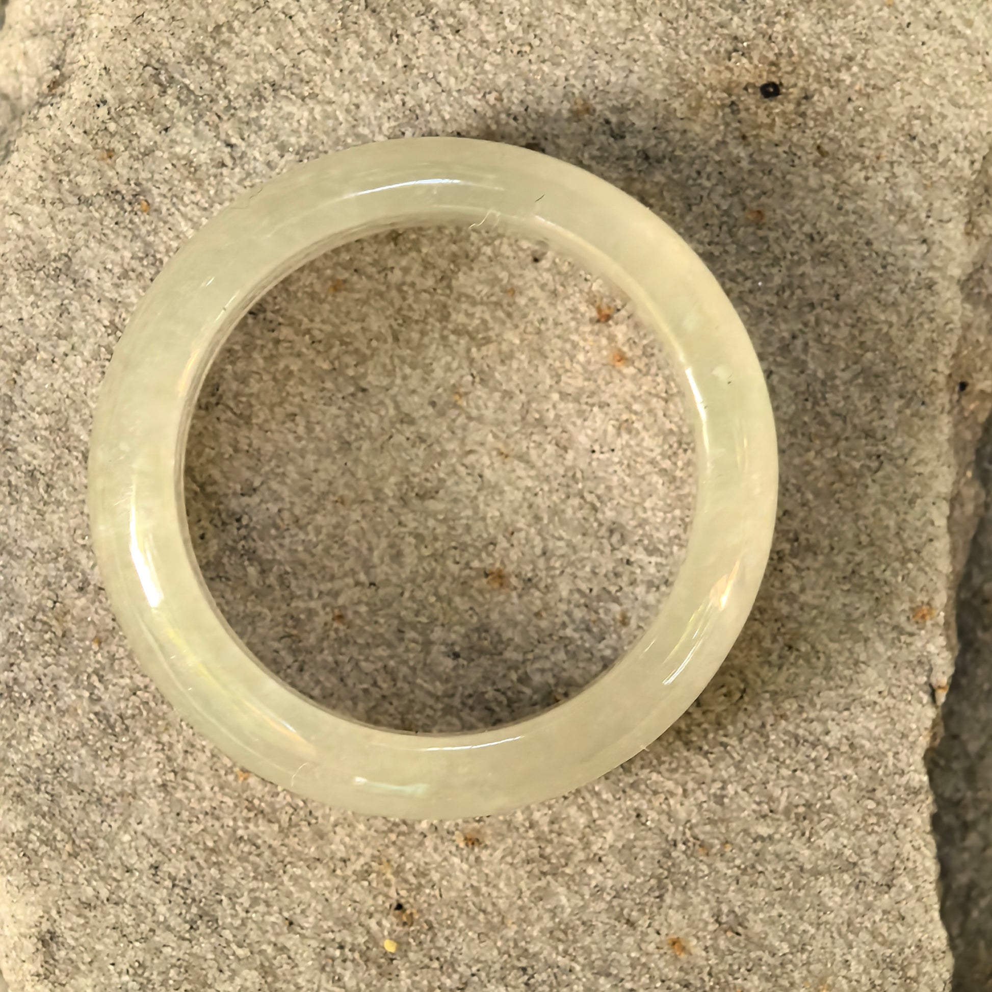 Natural Grade-A yellow jadeite ring band placed on stone surface, showing circular shape and icy glutinous texture.
