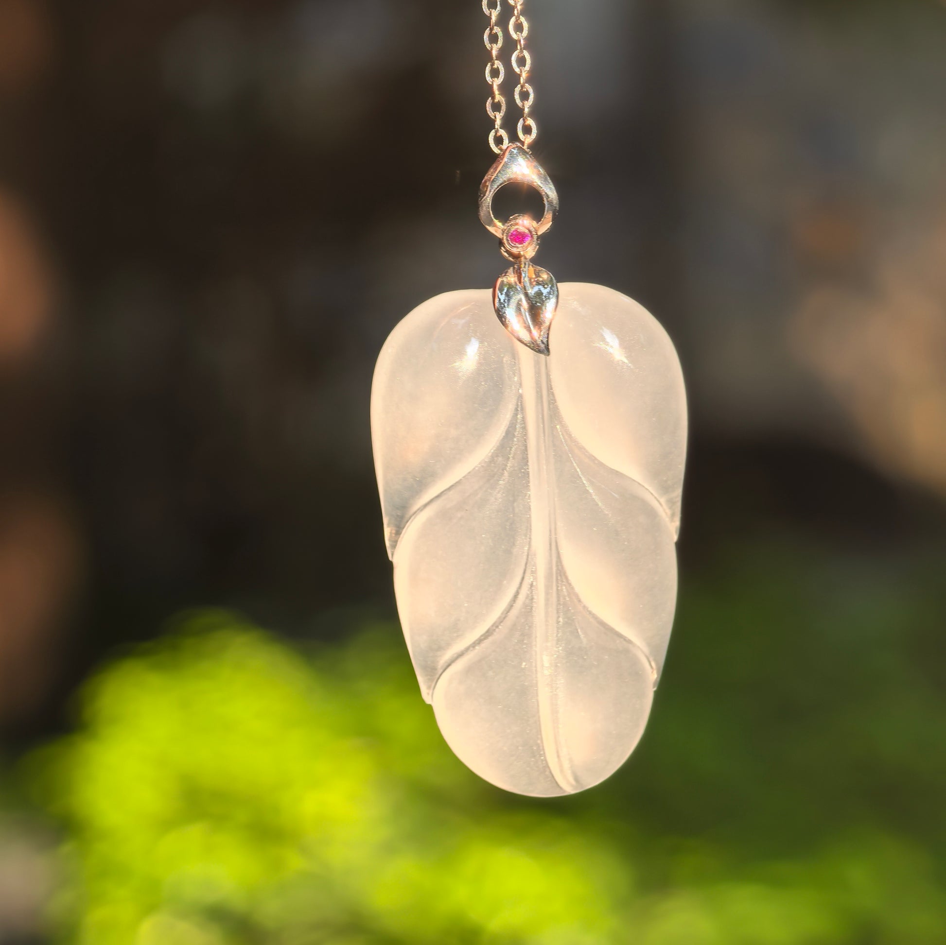 Natural Grade-A icy white jadeite leaf pendant with 18K gold setting hanging under natural light.