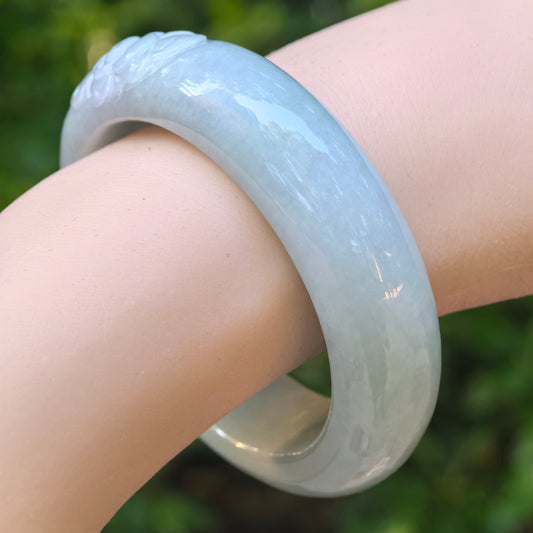 Natural Grade-A light green jadeite oval bangle worn on the wrist, showing its smooth polish and soft glutinous texture.