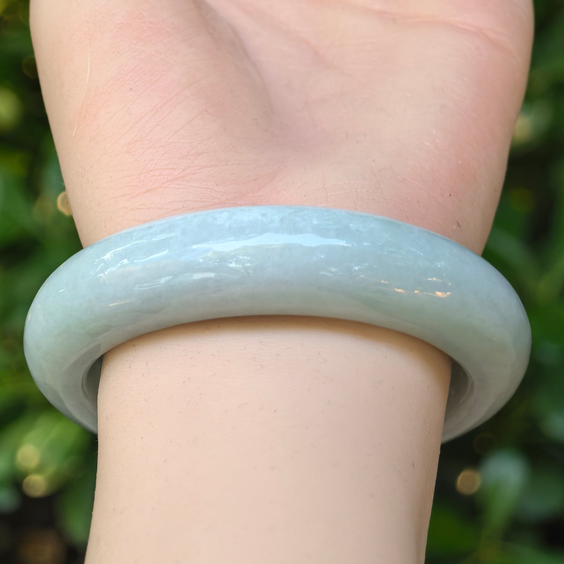 Side view of the carved lotus jadeite bangle worn on the wrist, showing its rounded shape and gentle luster.