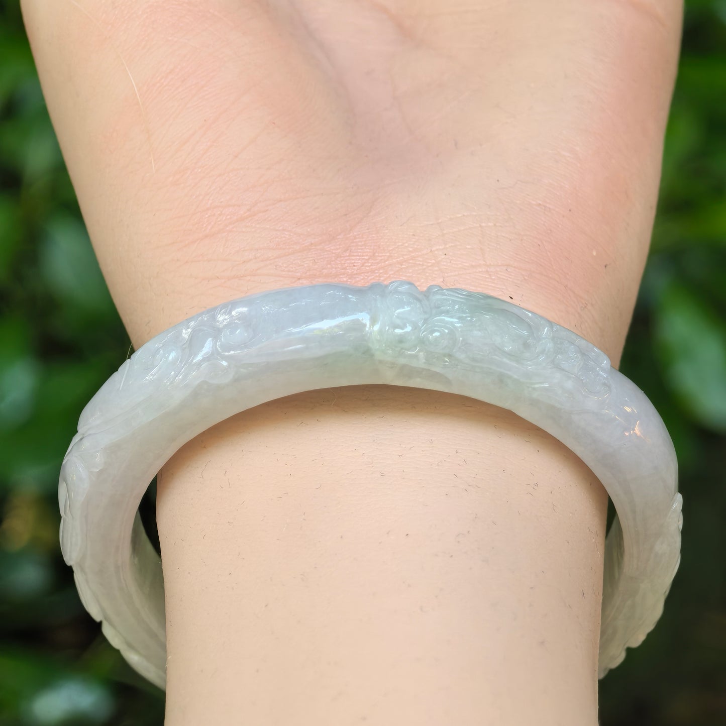 Close wrist view of a Natural Grade-A light green jadeite D-shape bangle with carved bat motifs.