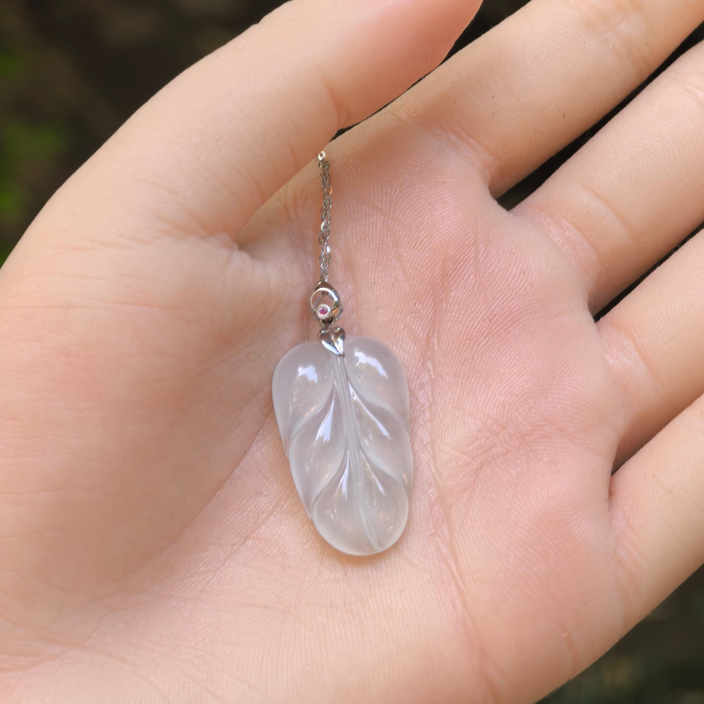 Natural Grade-A jadeite leaf pendant shown on hand for size reference.