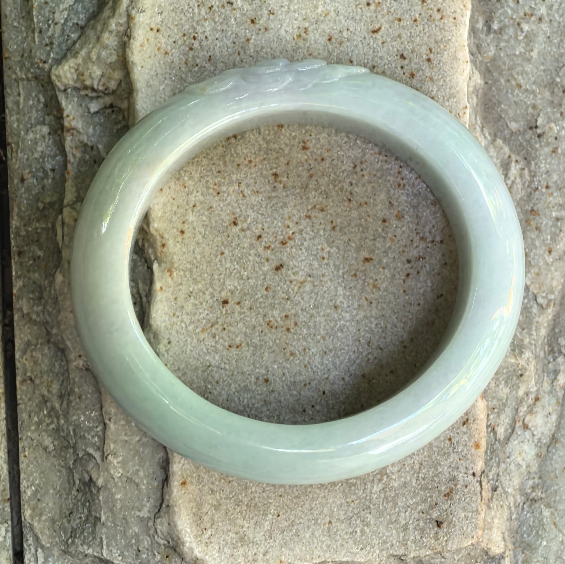 Natural light green jadeite oval bangle displayed on stone, showing the overall shape and polished finish.
