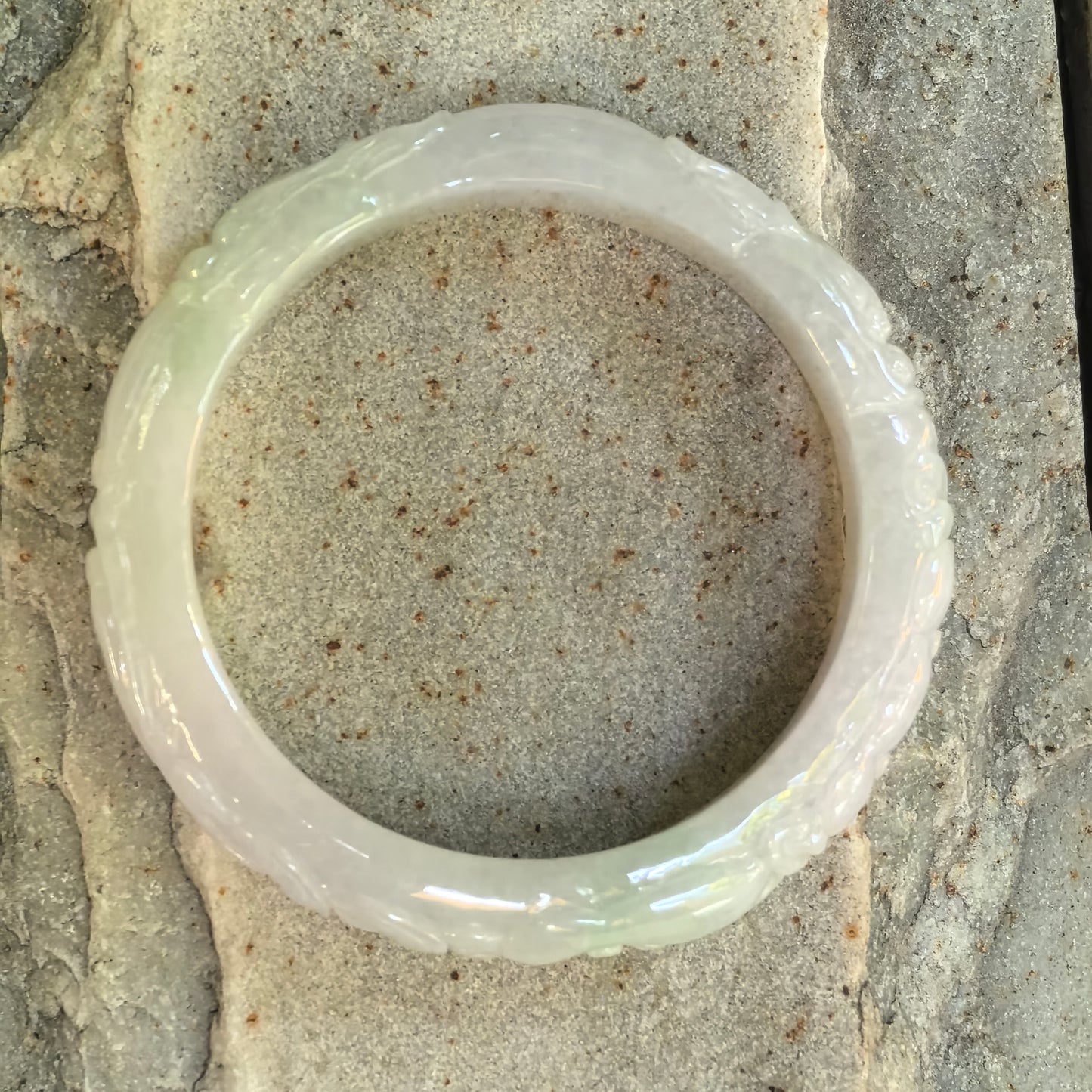 Full view of a Natural Grade-A light green carved jadeite D-shape bangle displayed on stone.