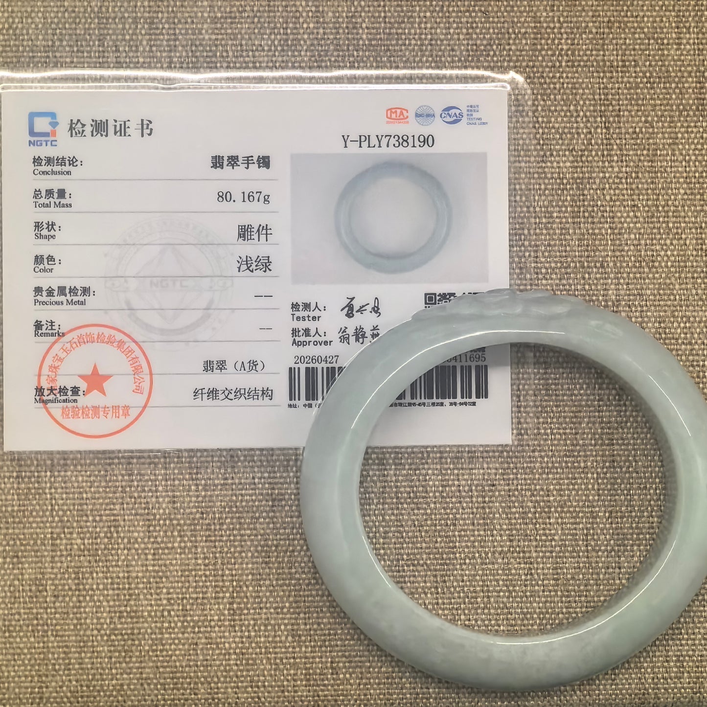 NGTC certified light green carved lotus jadeite oval bangle shown with its matching certificate.

