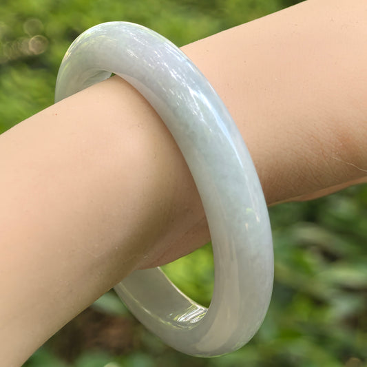 Natural Grade-A light green jadeite D-shape bangle worn on the wrist, showing its smooth polish and glutinous texture.