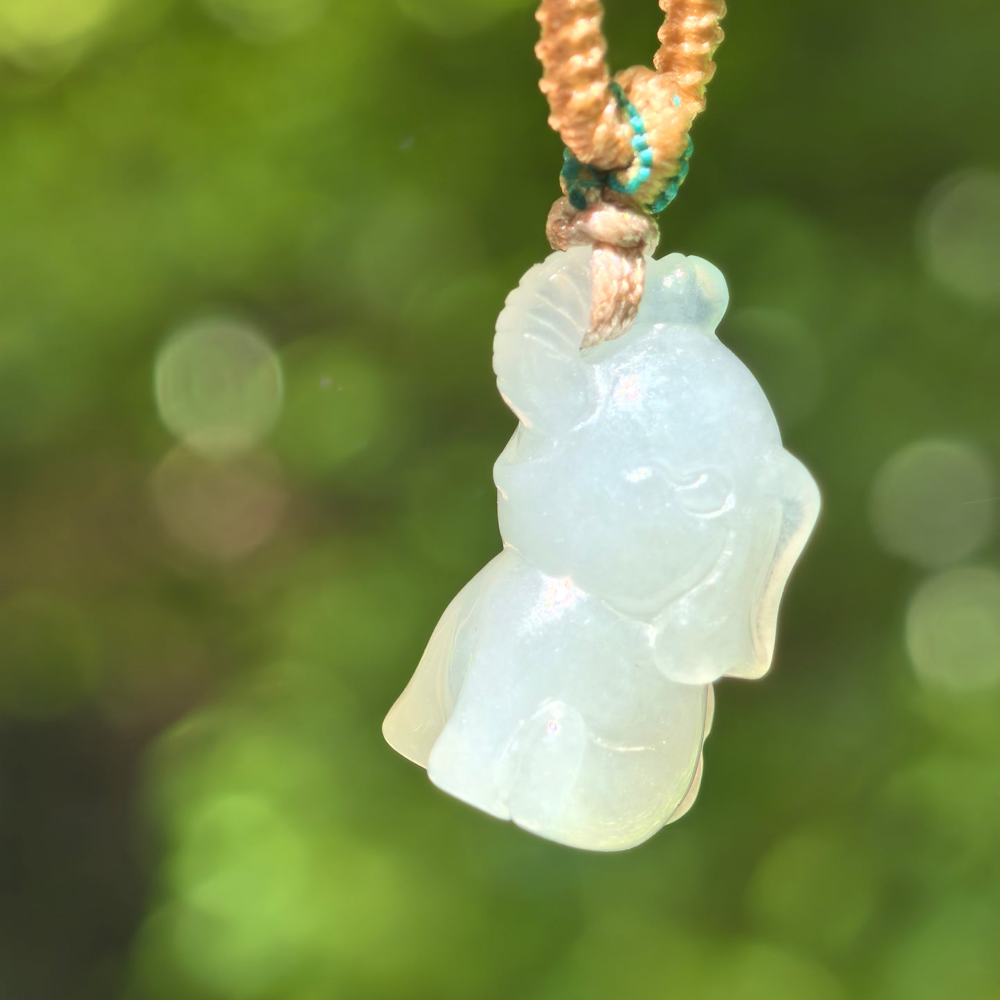 Natural Grade-A glutinous icy light green 3D elephant jadeite pendant hanging on cord, front view.