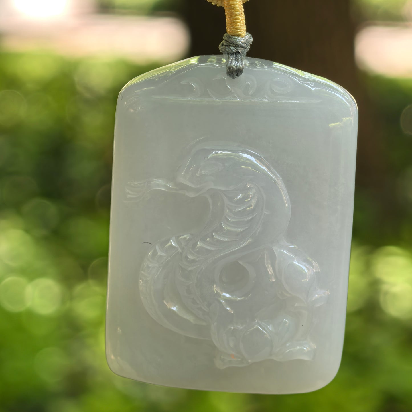 Close front view of a Natural Grade-A white jadeite rectangular pendant carved with a snake motif.