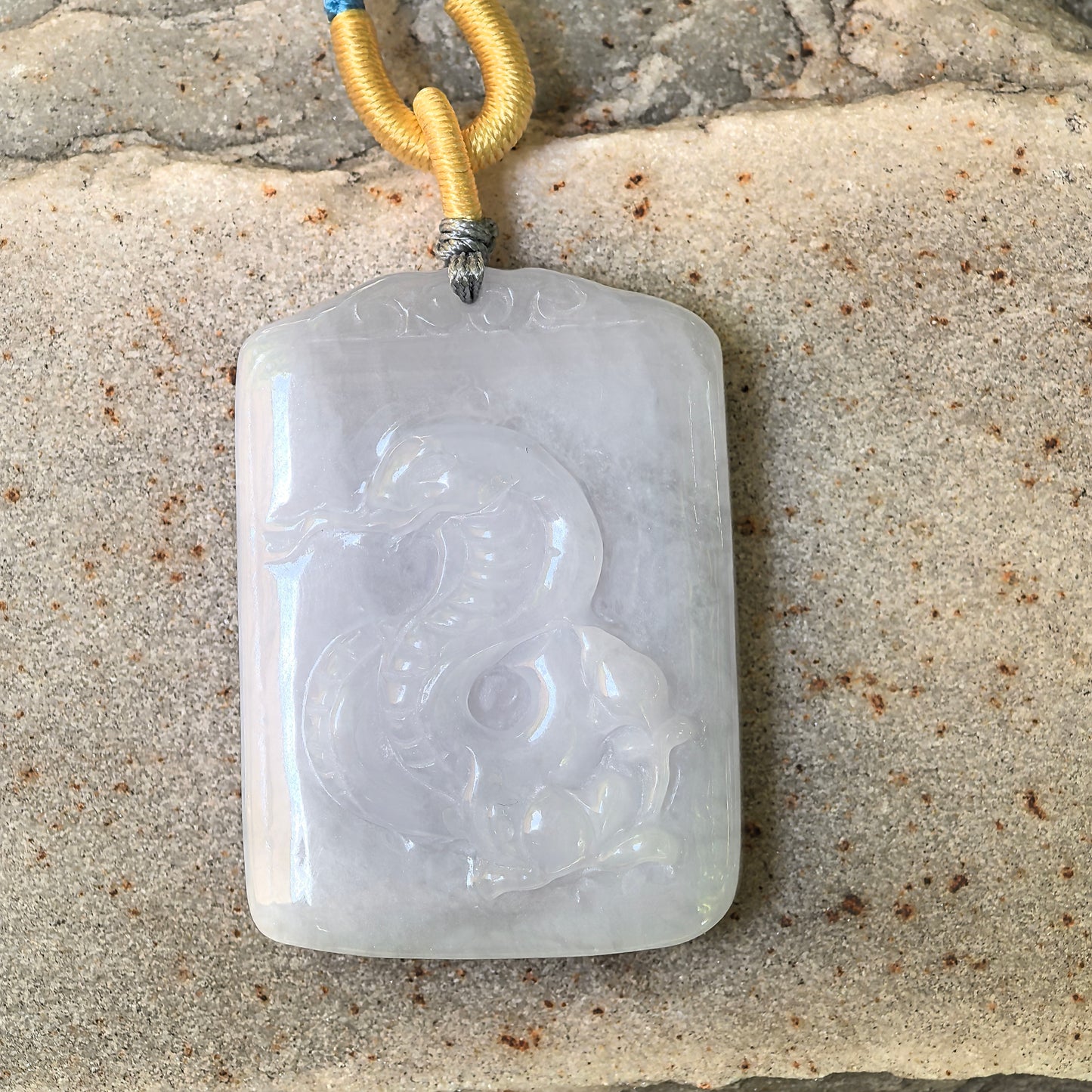 Natural Grade-A white jadeite snake pendant placed on stone background.