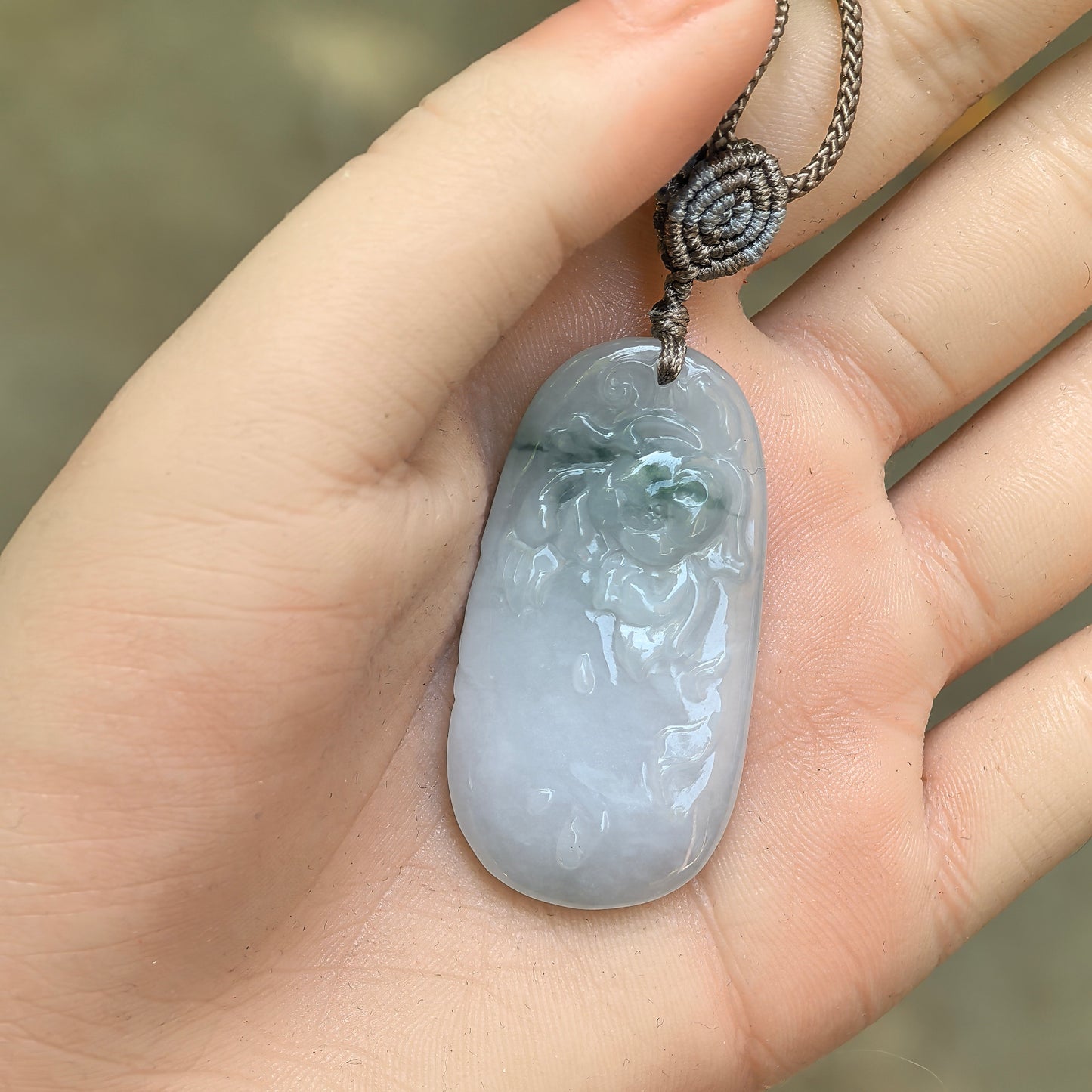 Close view of a Natural Grade-A glutinous floating green carved jadeite pendant held in hand.