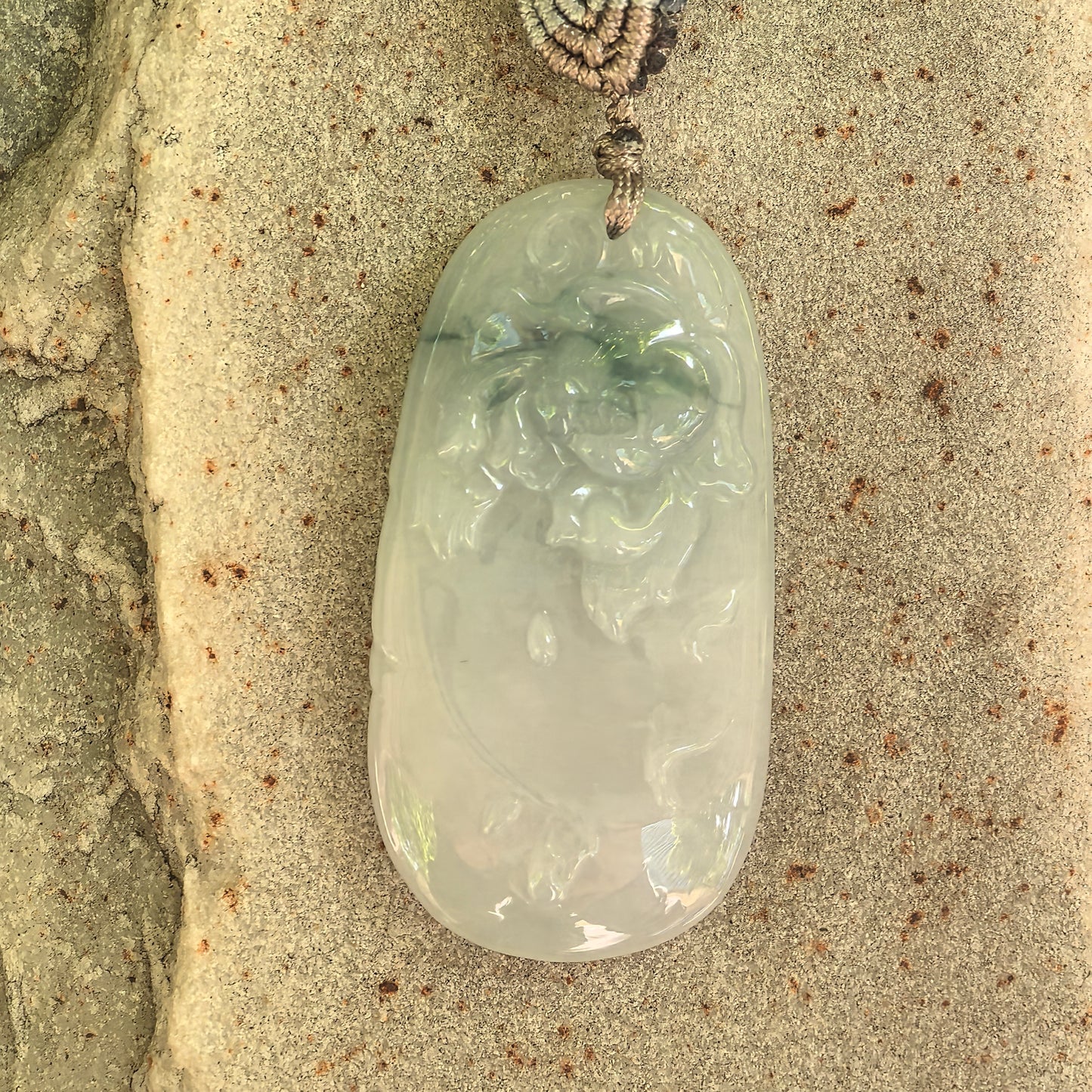 Natural Grade-A glutinous floating green carved jadeite pendant displayed on a stone surface.