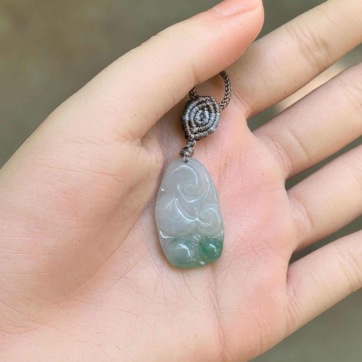 Petite carved Ruyi jadeite pendant held in hand, showing compact size and green accent.