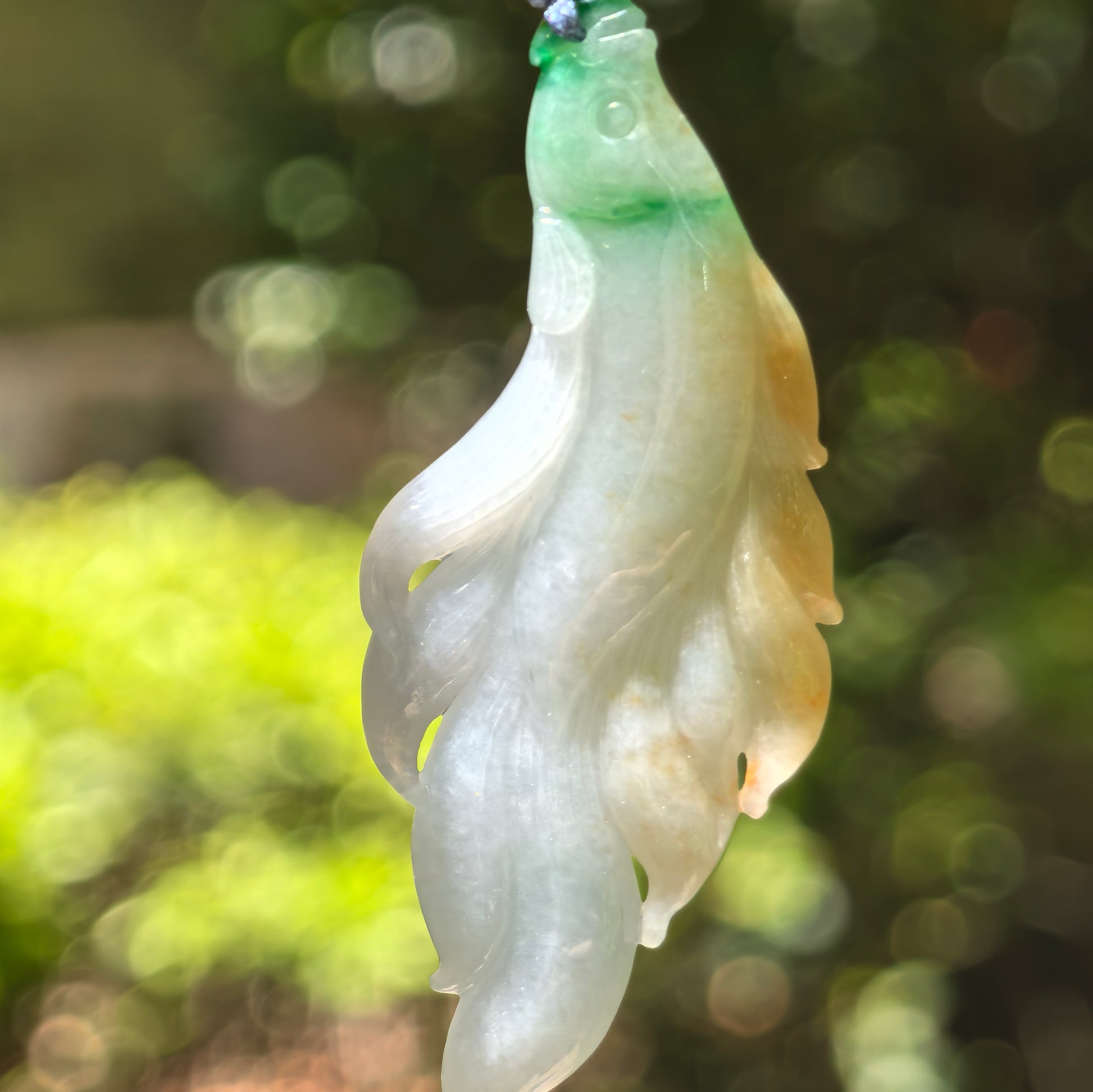 Close-up of yellow-green jadeite fish pendant showing vivid carved details.