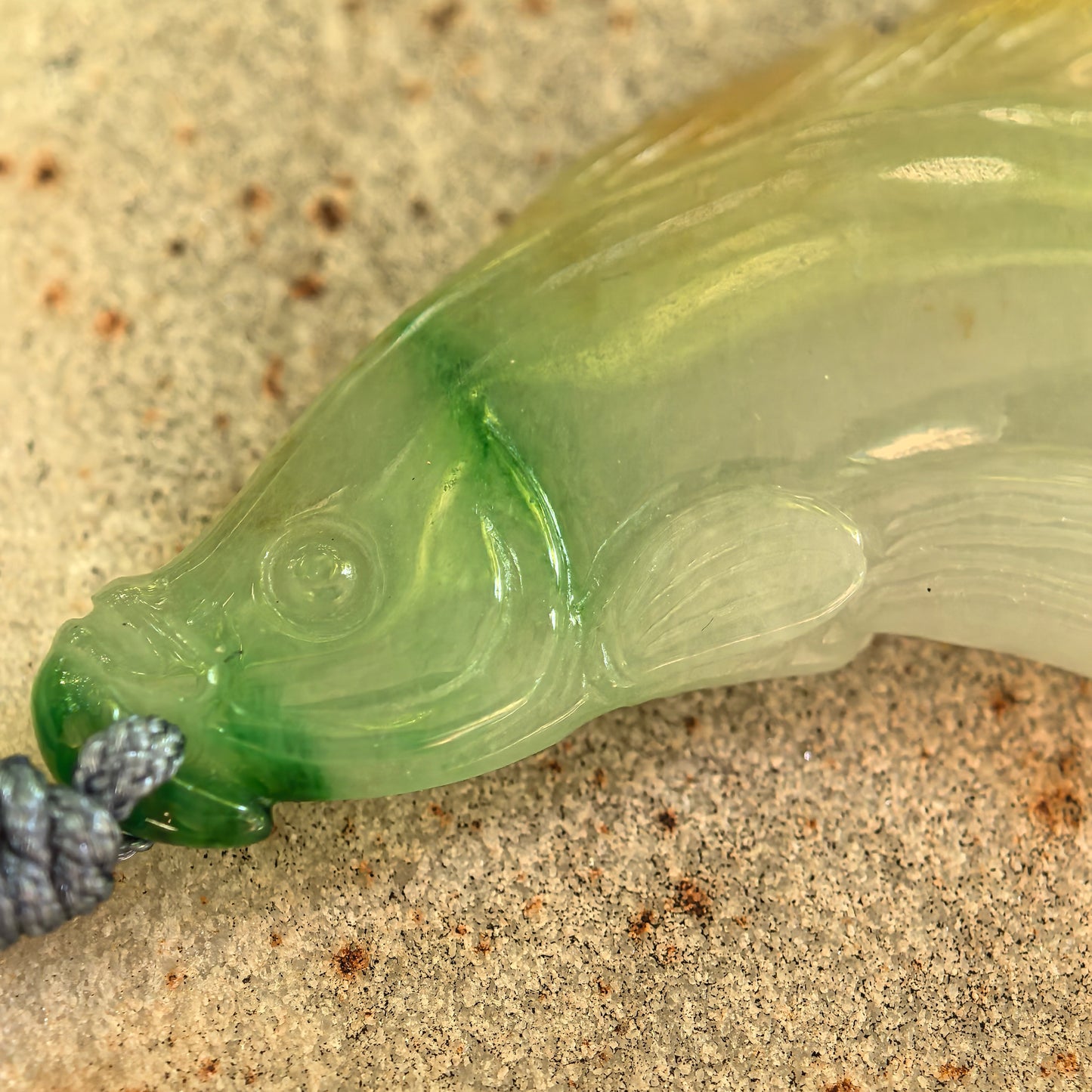 Glutinous yellow-green jadeite fish pendant displayed on stone background.