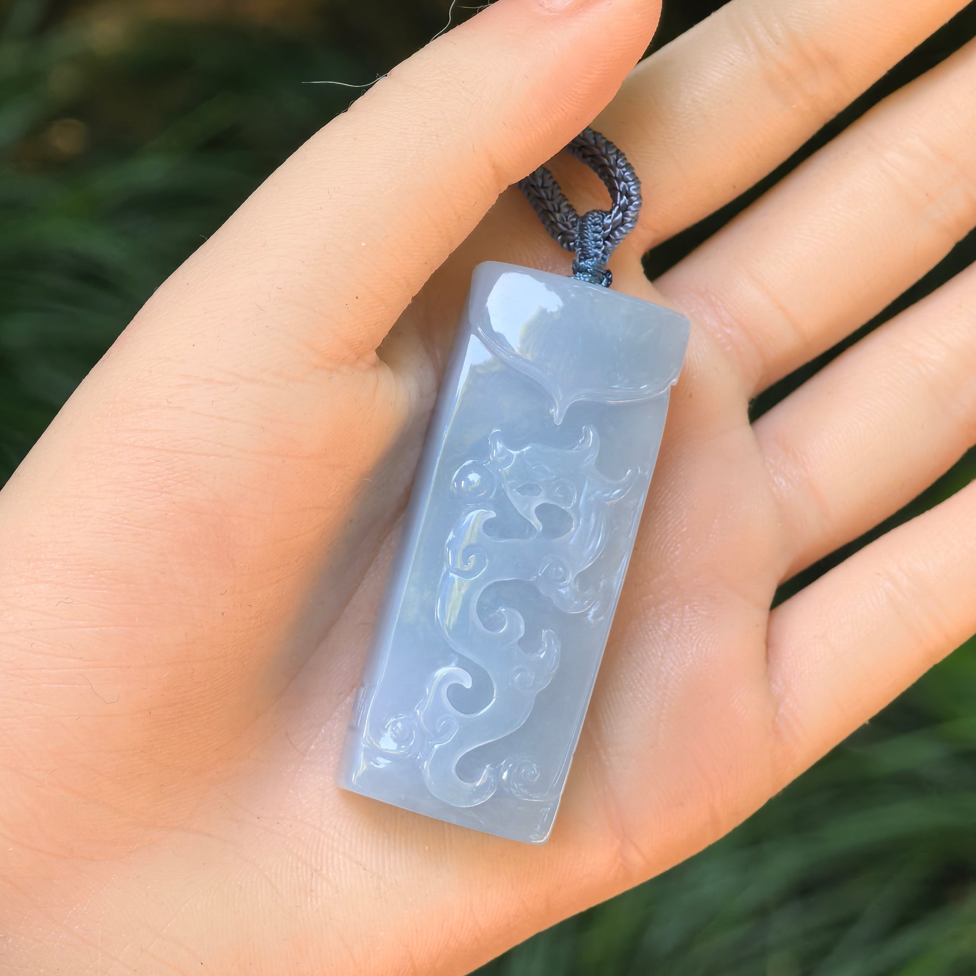 Natural Grade-A glutinous blue-lavender jadeite dragon pendant held in hand, showing its size and glossy surface.