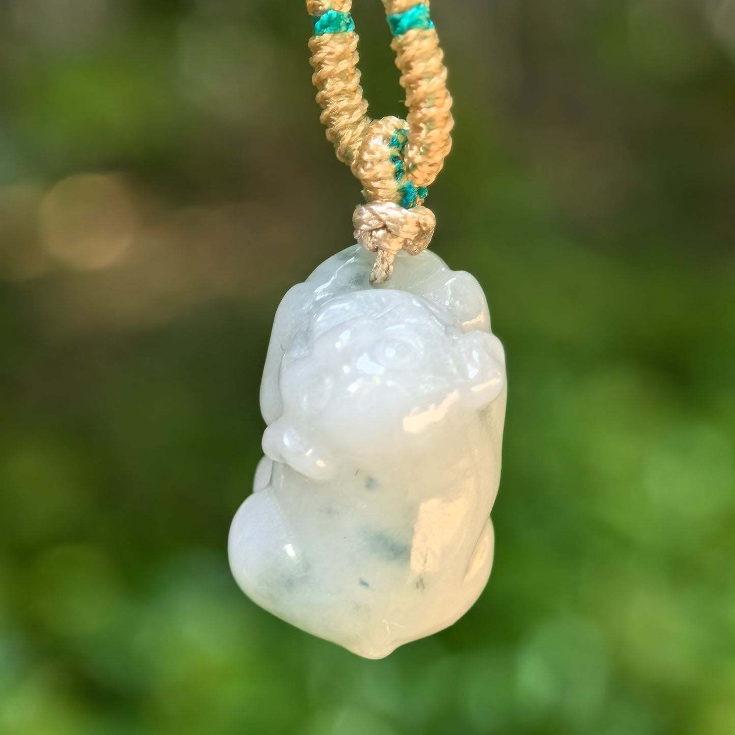 Natural Grade-A pig jadeite pendant hanging in natural light, showing a rounded three-dimensional carving and soft pale tone.