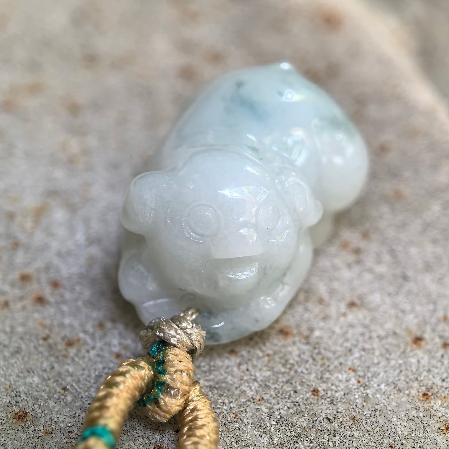 Natural Burmese jade pig pendant displayed on stone, highlighting its cute carving and glossy finish.