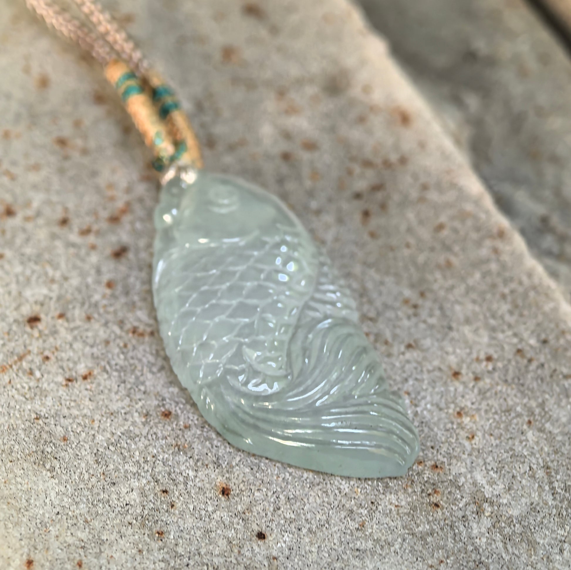 Icy translucent fish jadeite pendant resting on stone surface
