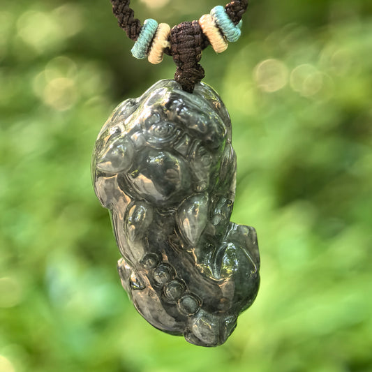 Natural Grade-A black chicken Pixiu jadeite pendant hanging in natural light, showing the three-dimensional carving and dark marbled tone.