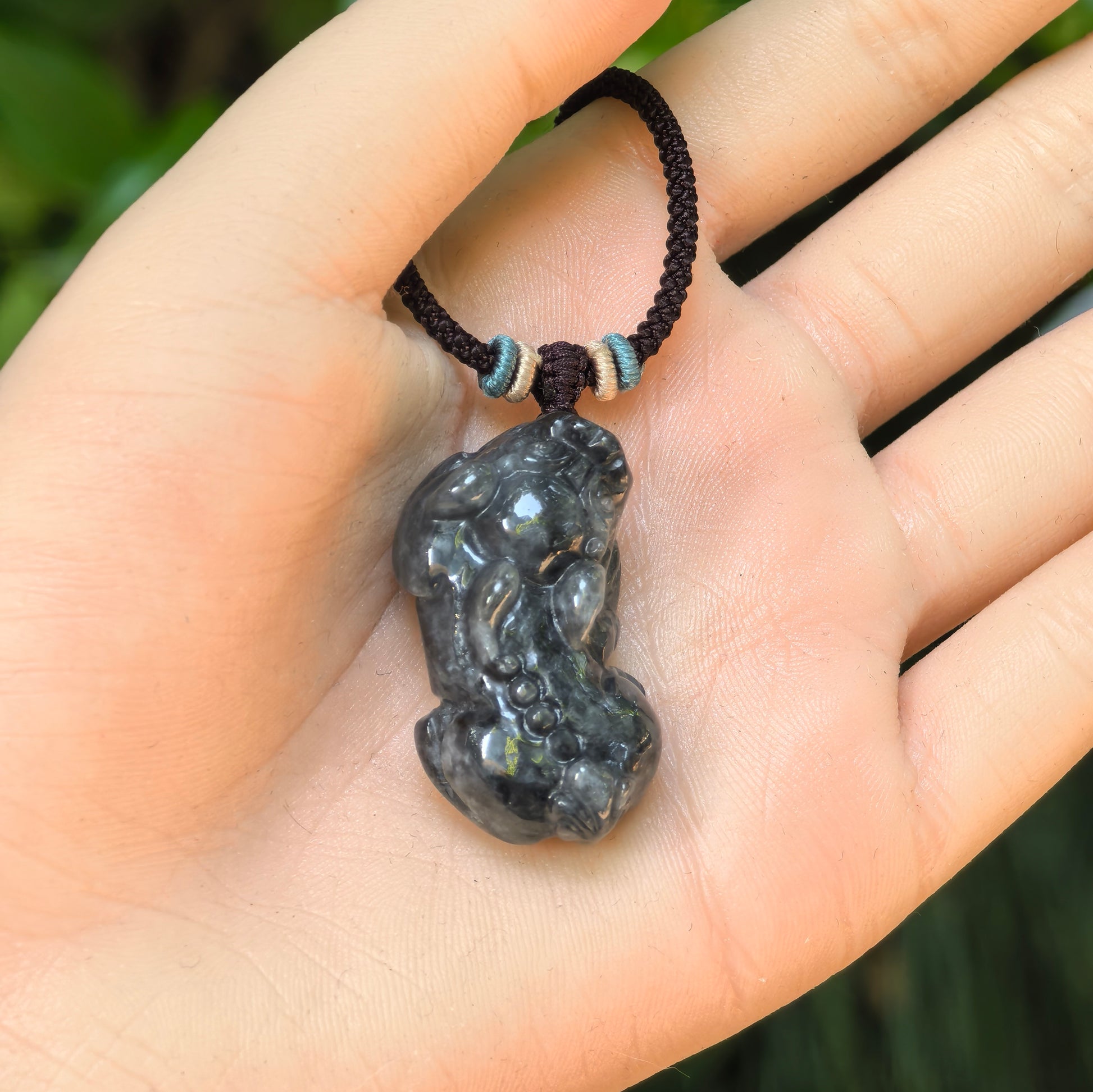 Black chicken Pixiu jadeite pendant shown in hand for size reference, highlighting its thick and compact form.