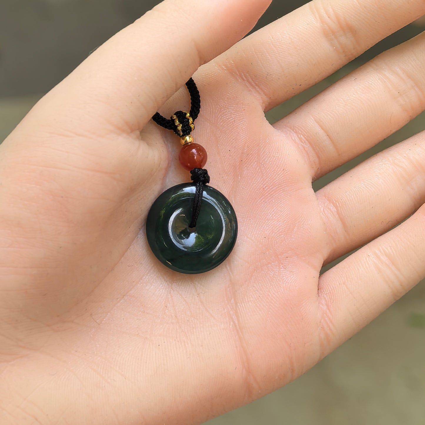 Handheld deep teal blue jadeite Peace Pendant showing compact size, curved surface, and central opening.

