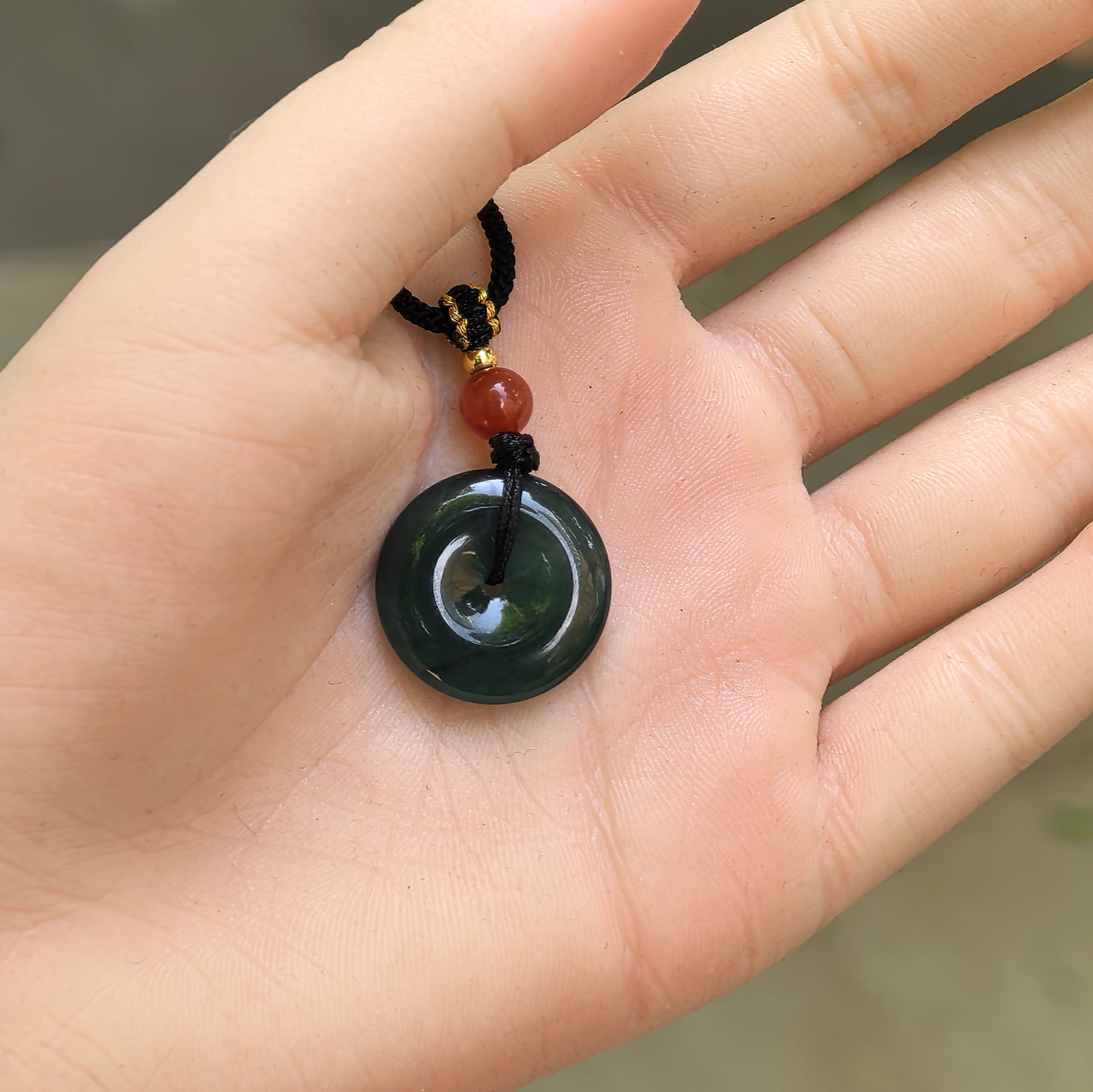 Handheld deep teal blue jadeite Peace Pendant showing compact size, curved surface, and central opening.
