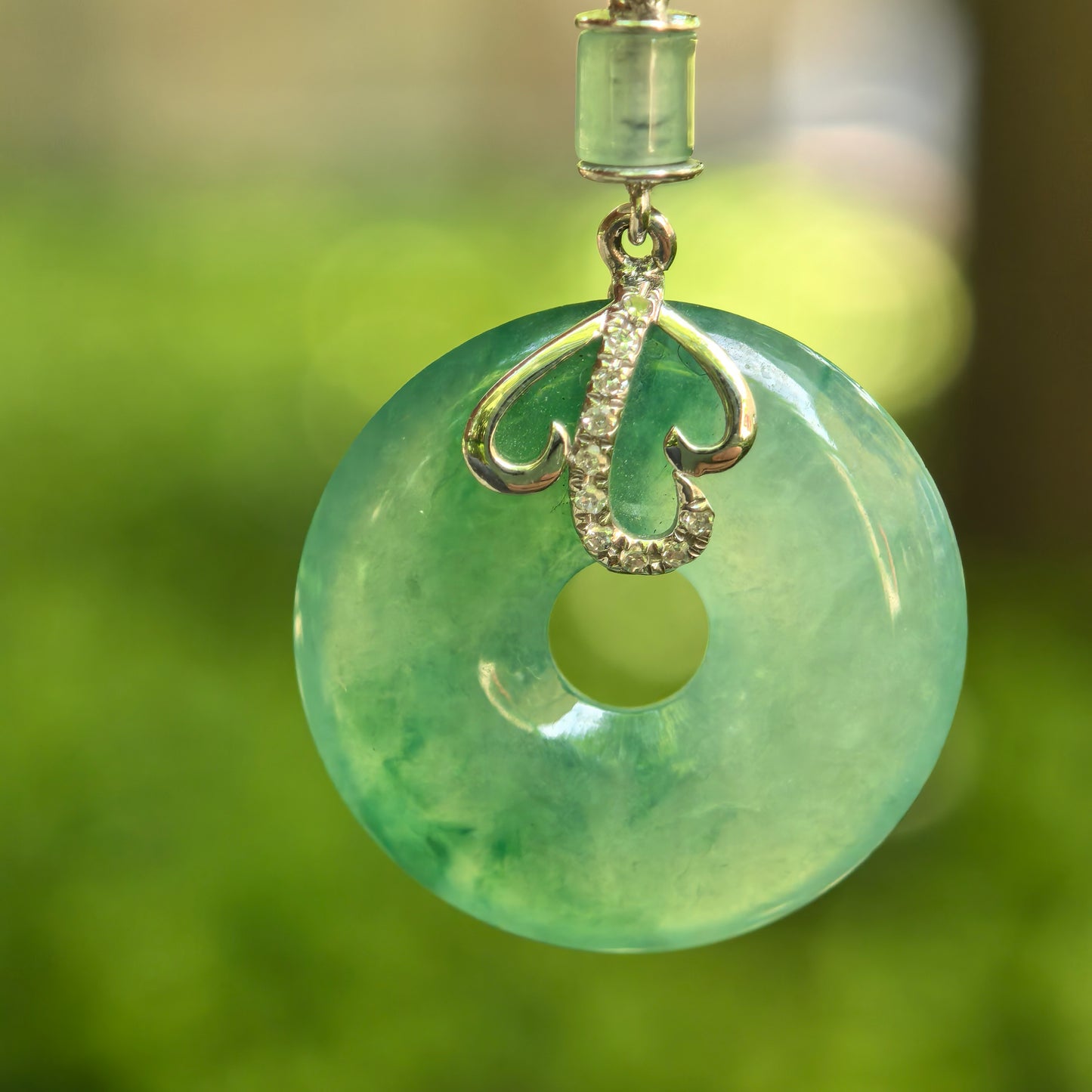 Natural Grade-A icy glutinous green donut jadeite pendant with 18K gold and diamond accents hanging outdoors.
