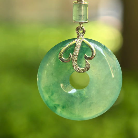 Natural Grade-A icy glutinous green donut jadeite pendant with 18K gold and diamond accents hanging outdoors.

