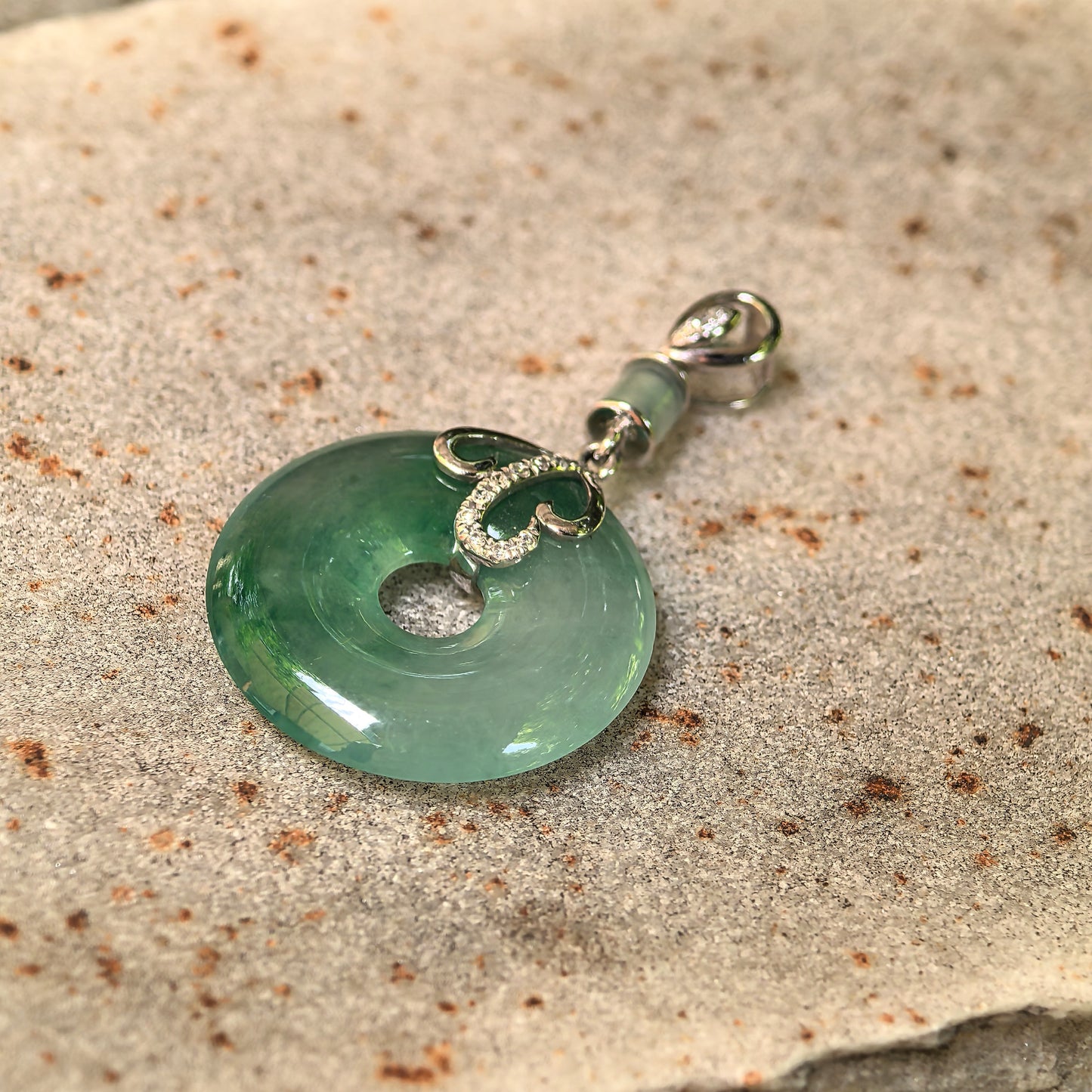 Close-up of green jadeite donut pendant showing round ring shape, central opening, and 18K gold setting.
