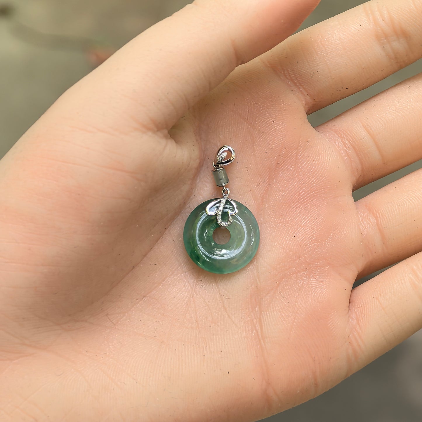 Handheld icy glutinous green jadeite donut pendant showing petite size and polished round shape.

